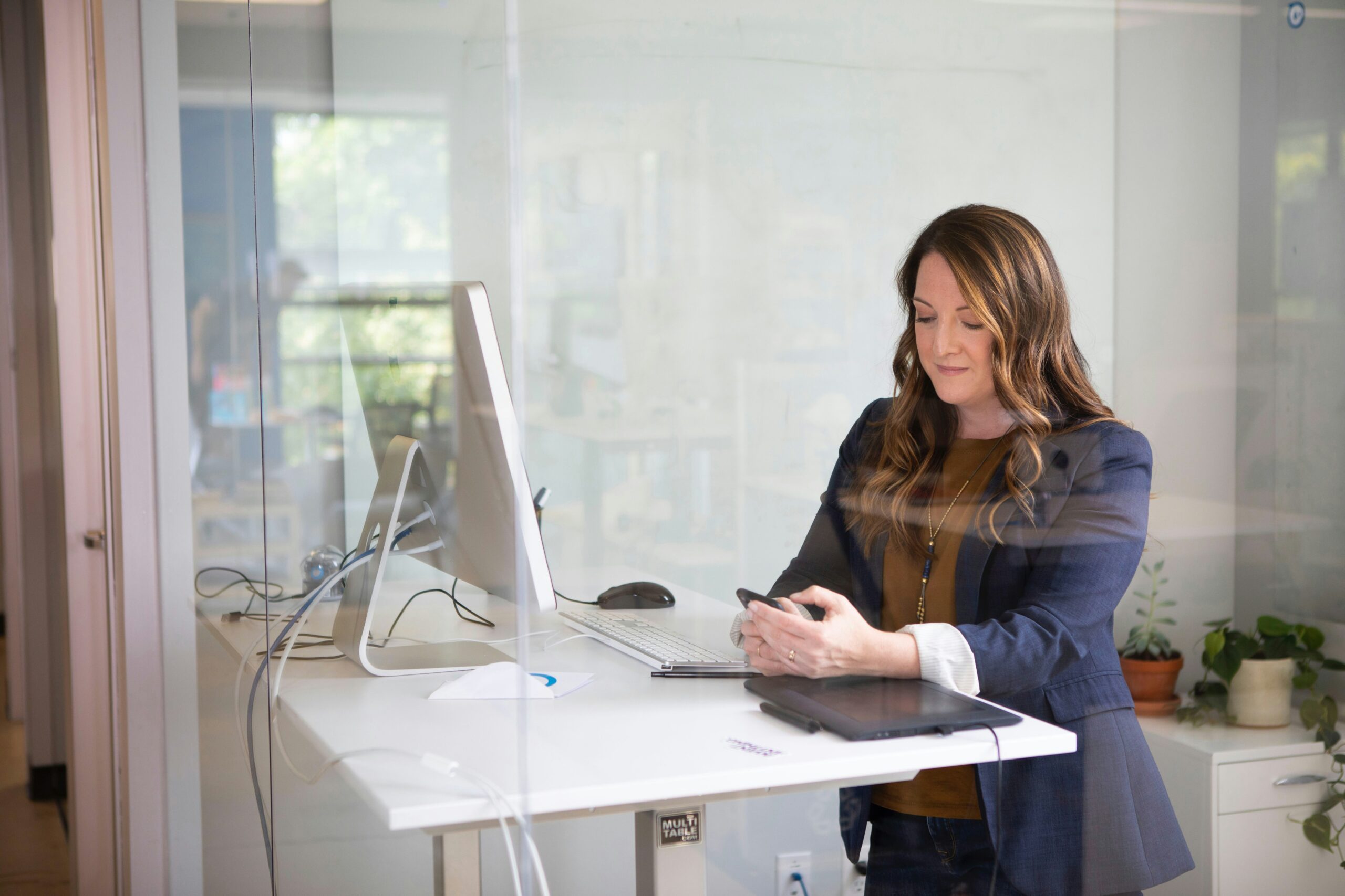 A woman on a stand-up desk checking her phone. 