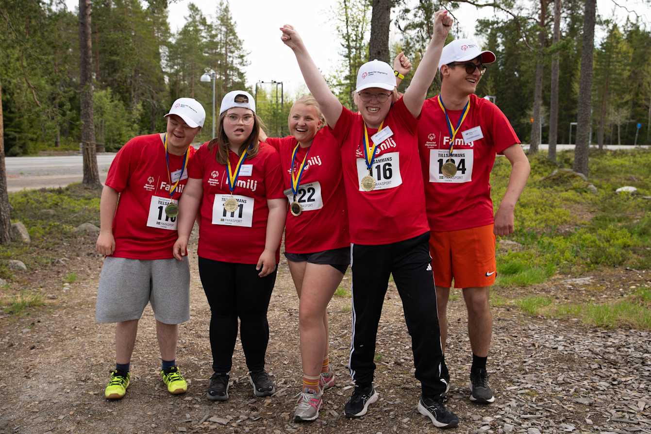 Utomhusmiljö, skogsbryn. Fem ungdomar poserar för kameran med sina medaljer. Alla har röda lägertröjor.