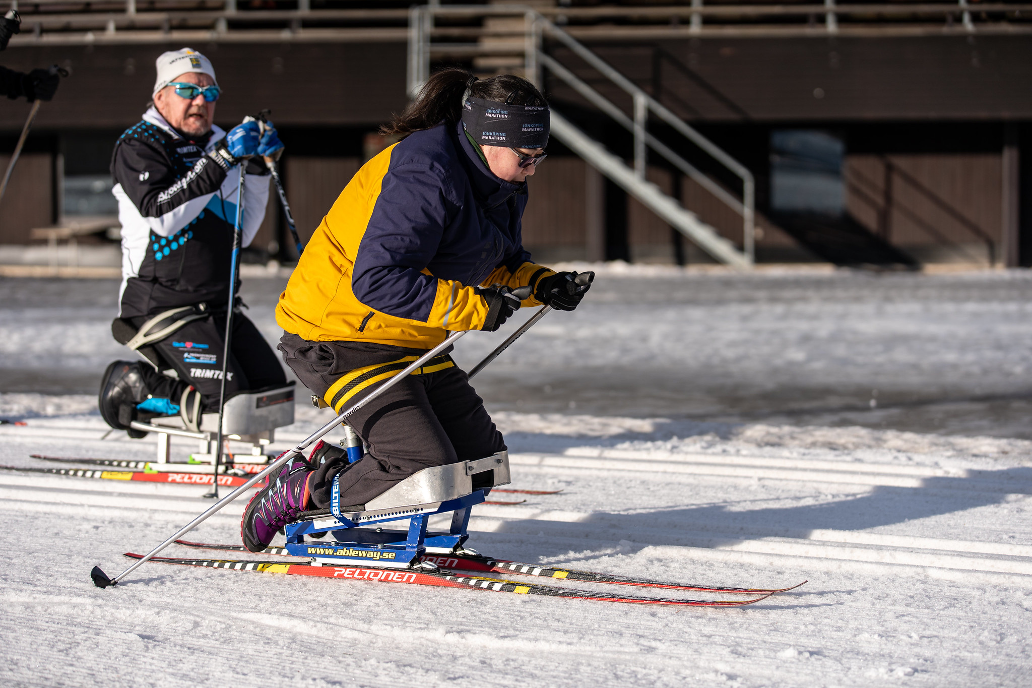 Kvinna på sitski stakar sig genom stadion. Solen skiner.