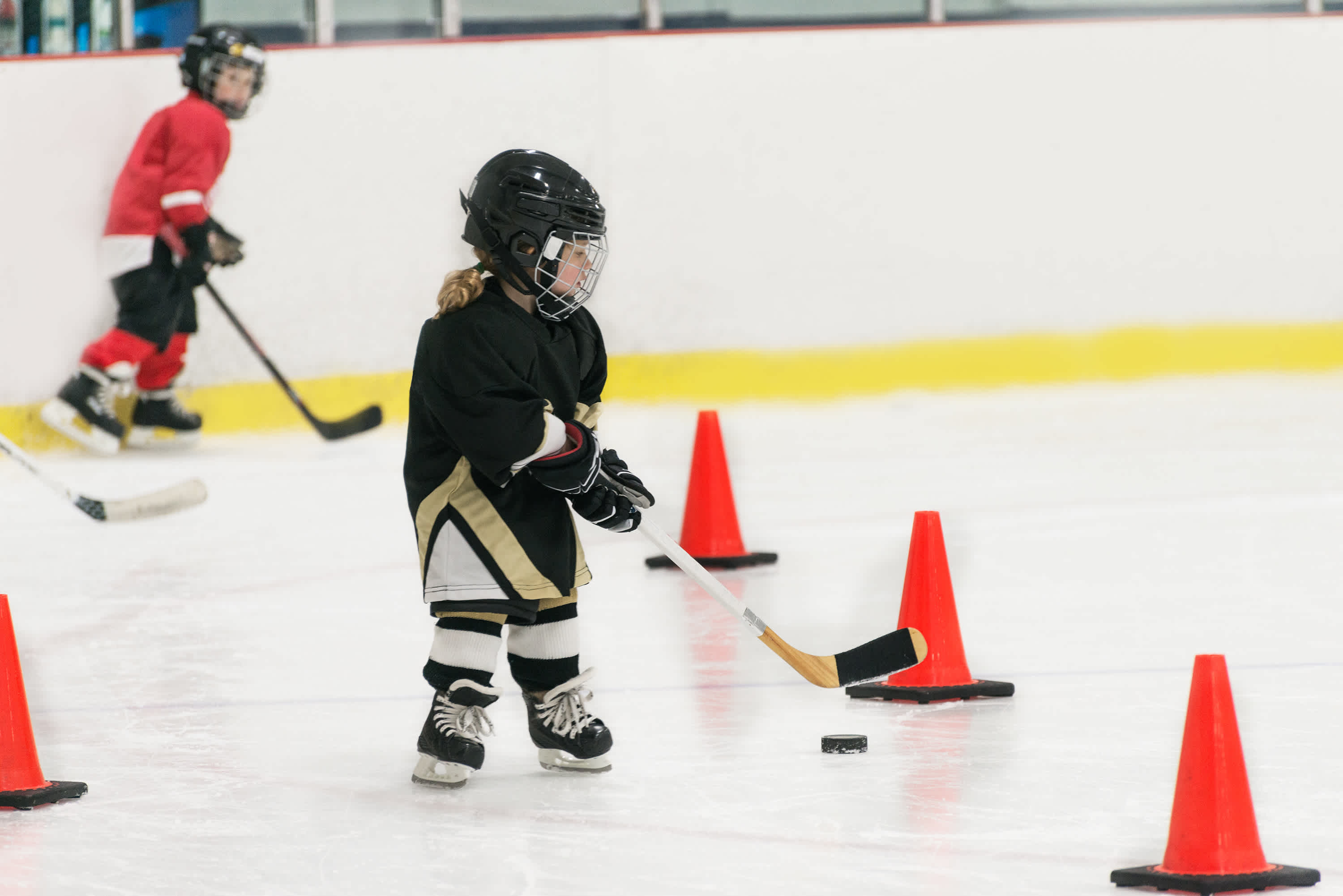 En tjej i ishockeyutrustning åker slalom mellan koner med ishockeyklubba och puck.