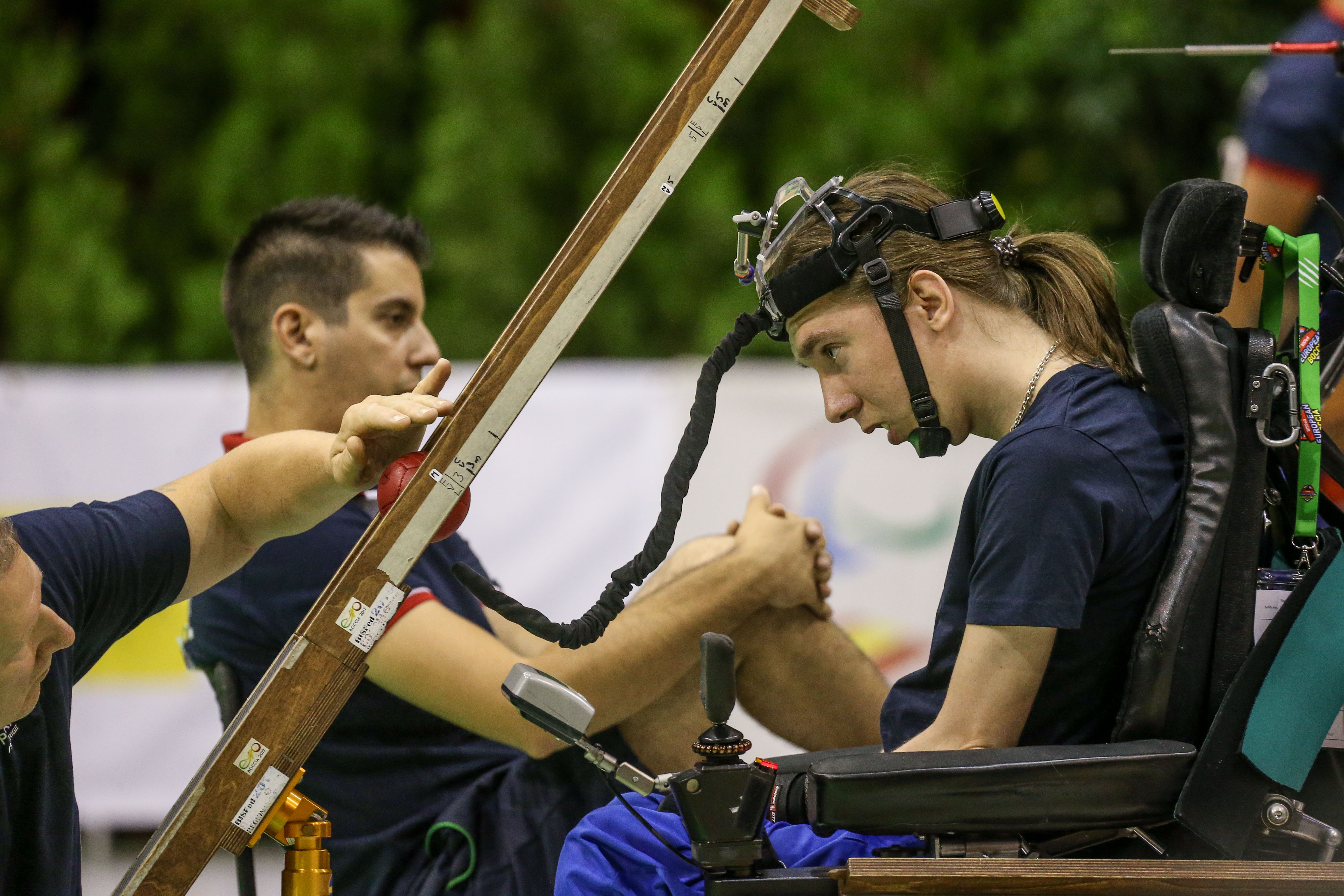 En ung man spelar boccia med en ränna. Han har en assistent som lägger bollen rätt.