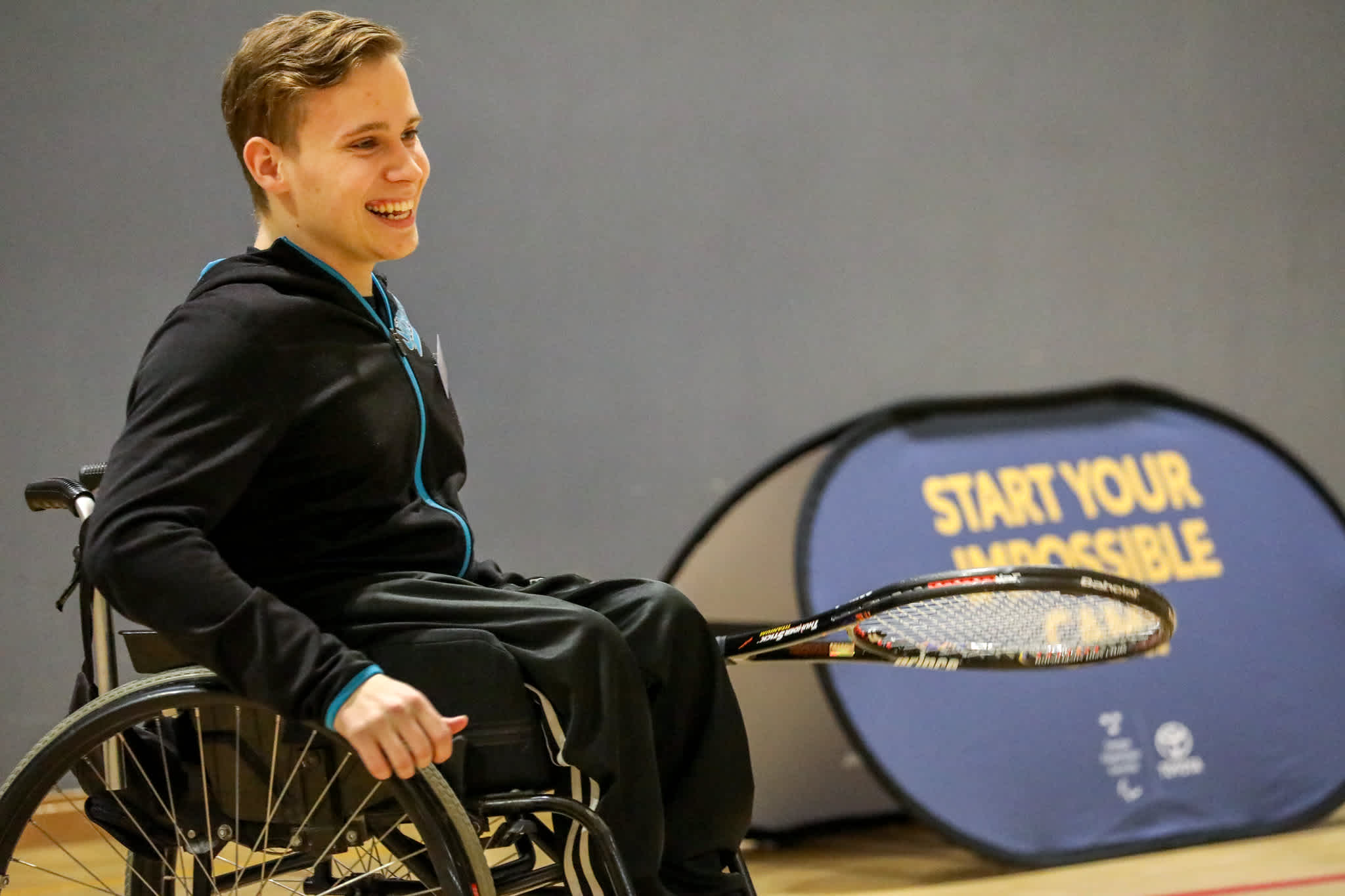 En kille i rullstol håller i ett tennisracket och ler mot sin motspelare