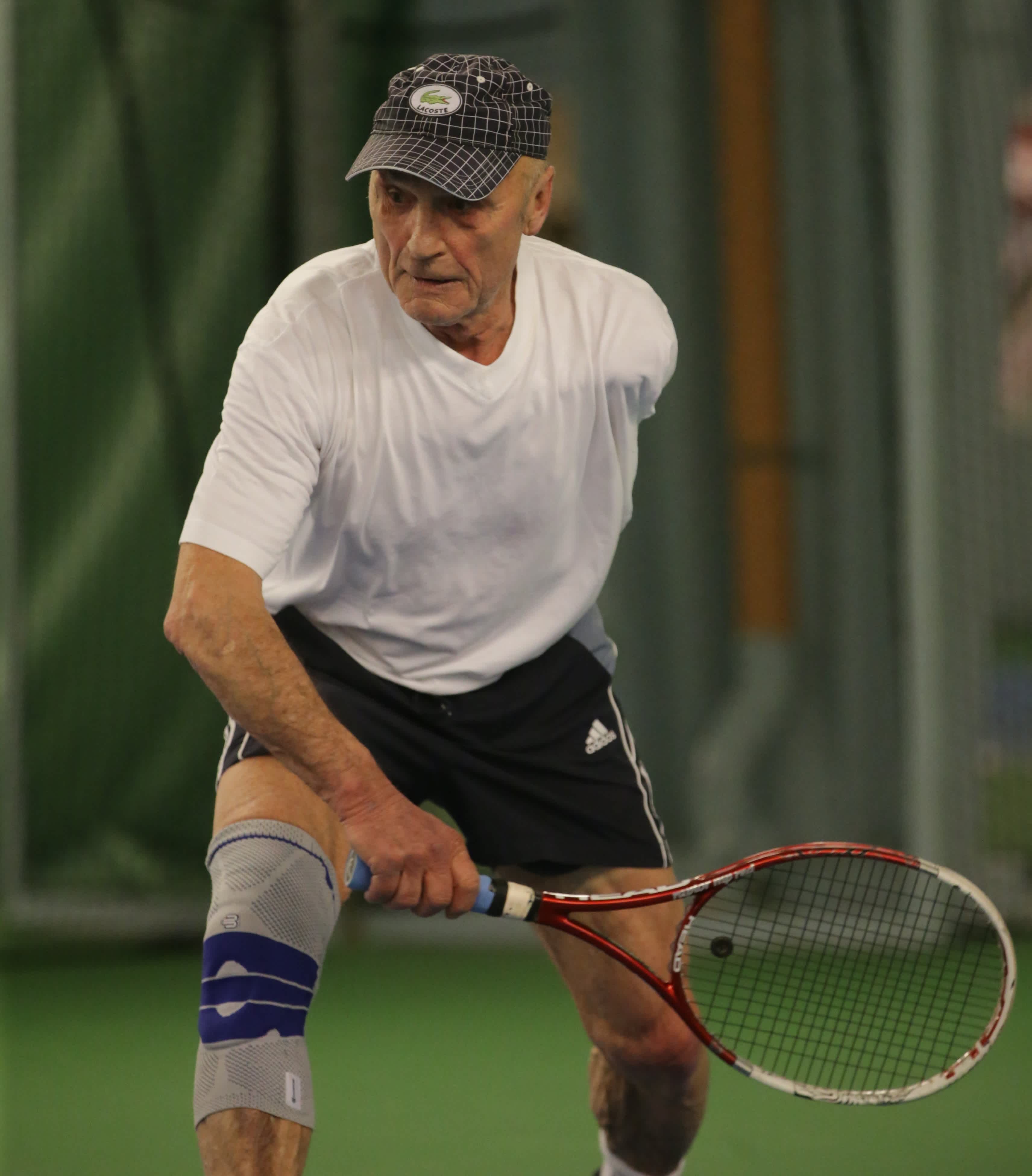 En äldre man spelar tennis.