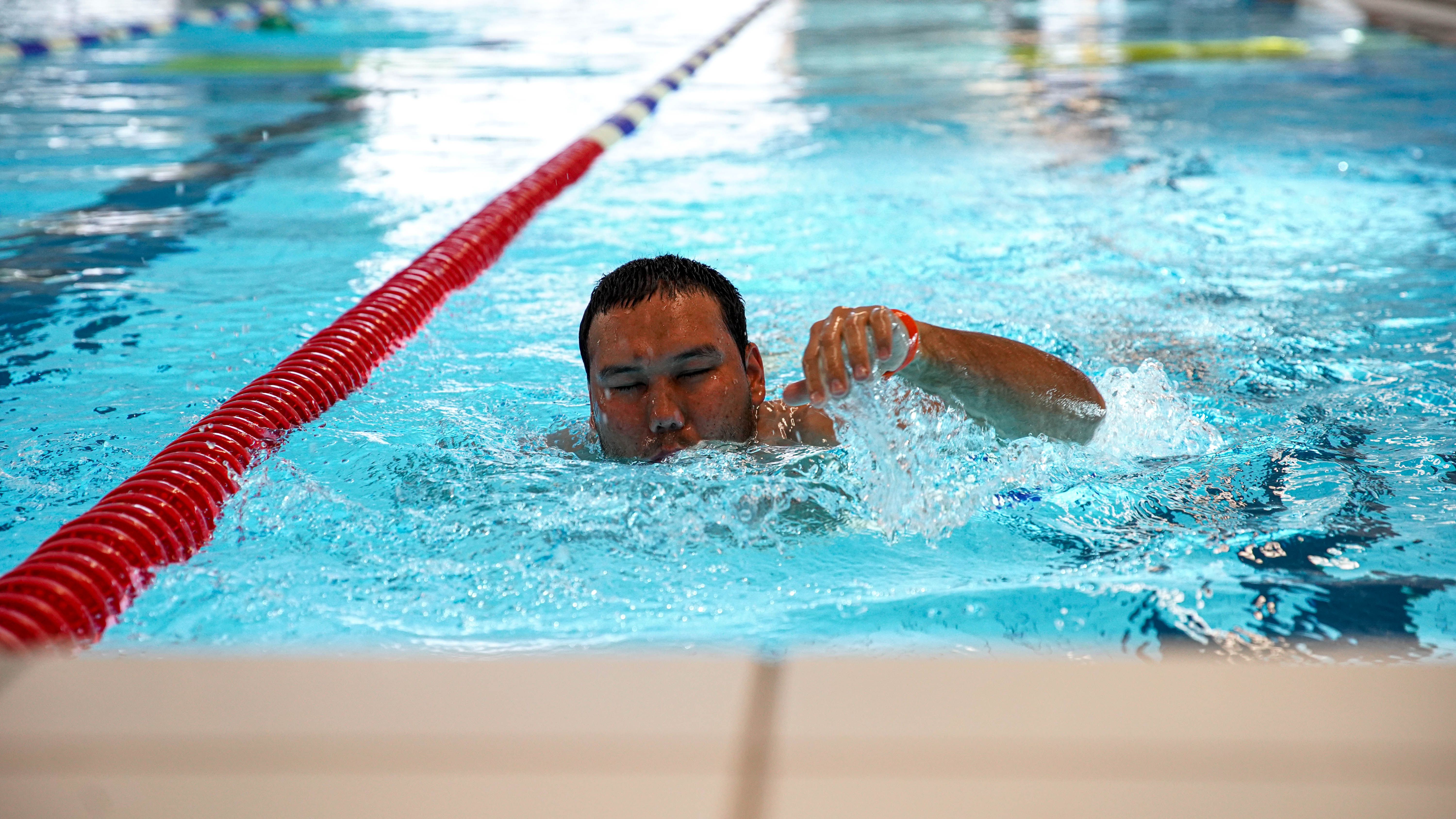 Man med synnedsättning simmar crawl i en bassäng inomhus.