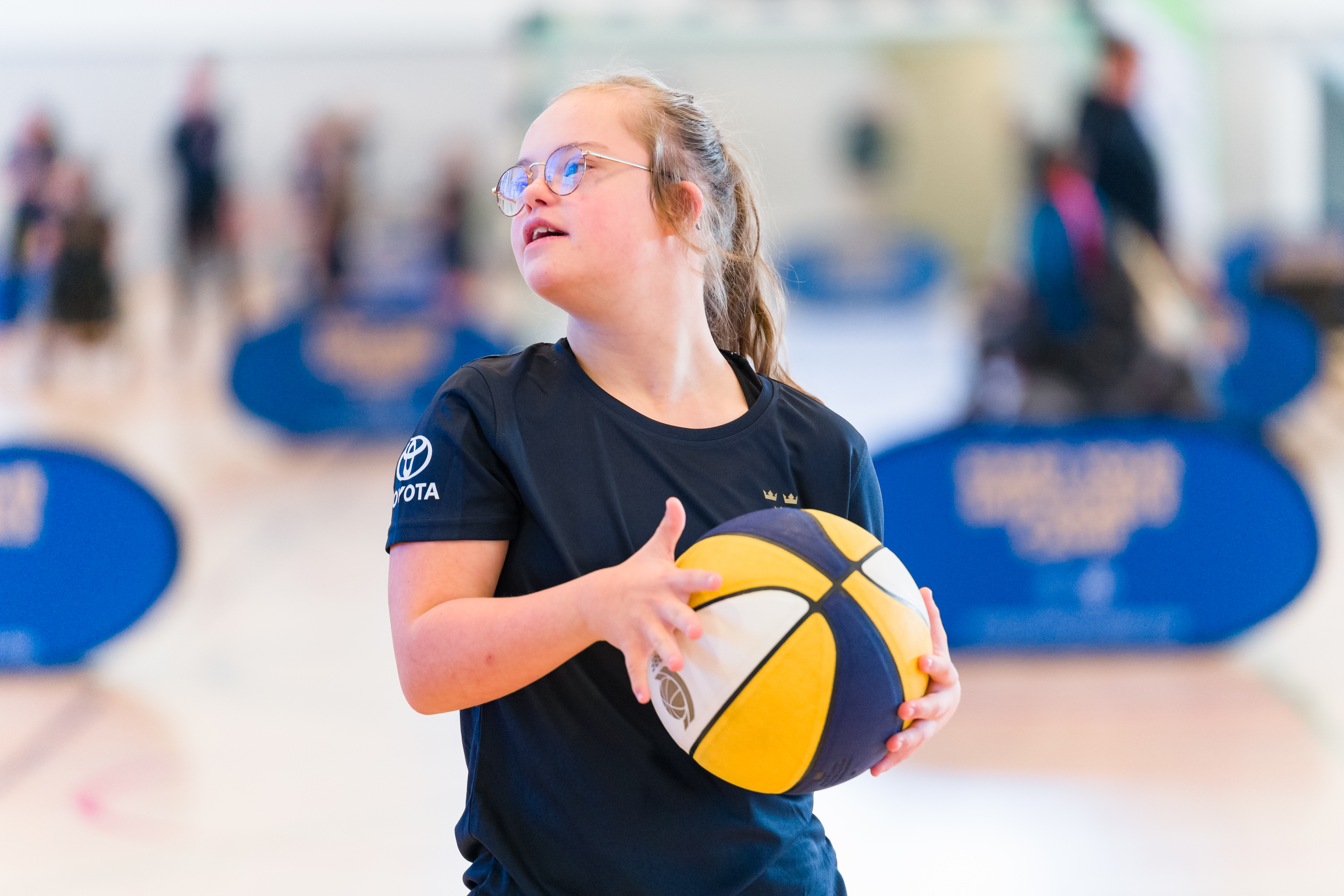 Flicka med basketboll i händerna tittar åt sidan.