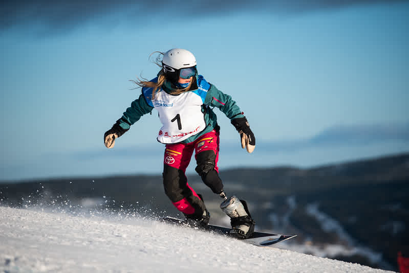 En kvinna åker snowboard. Hon har en protes på ena benet.
