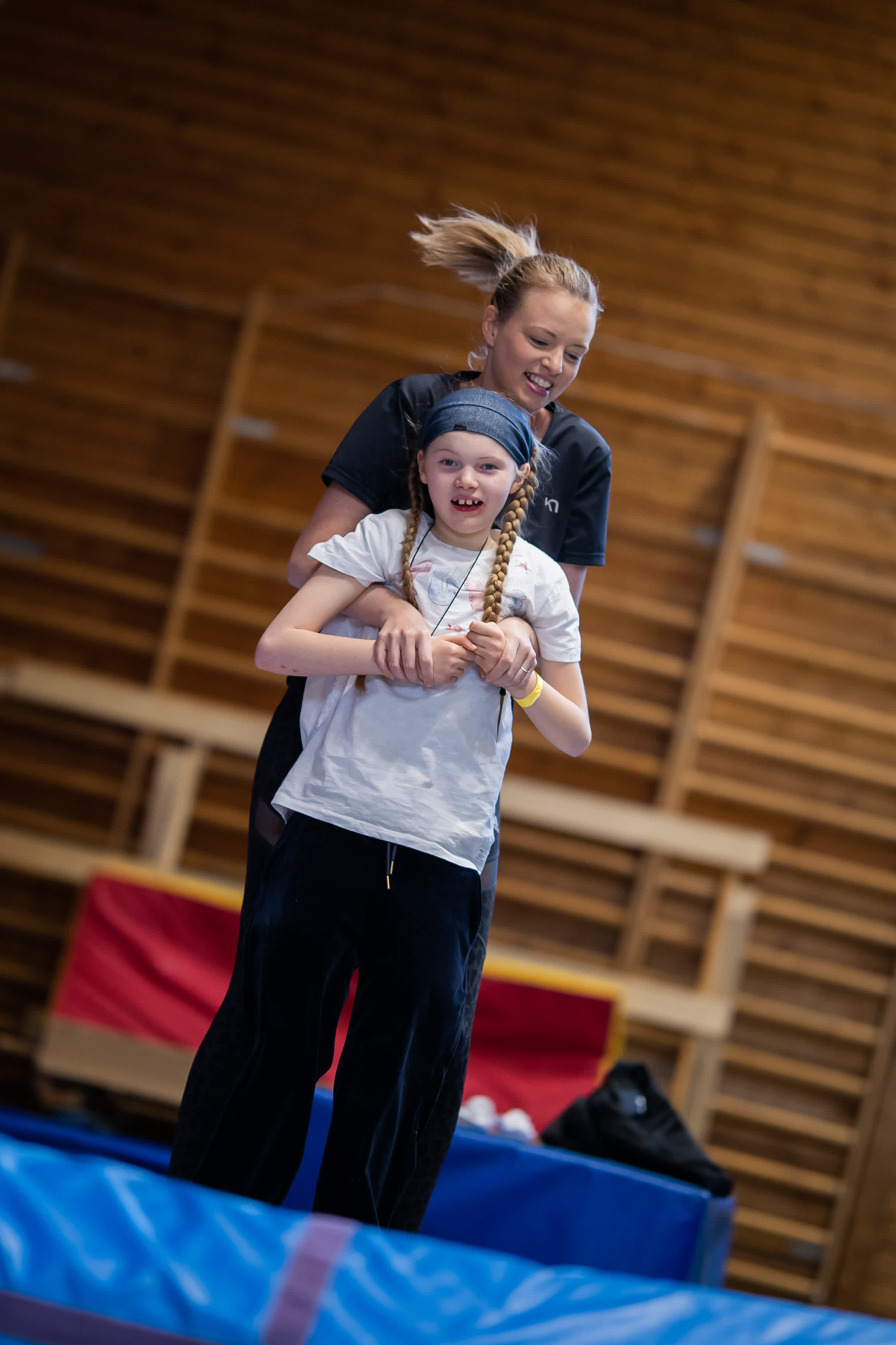 Flicka utövar gymnastik på trampolin, hoppar tillsammans med ledare.