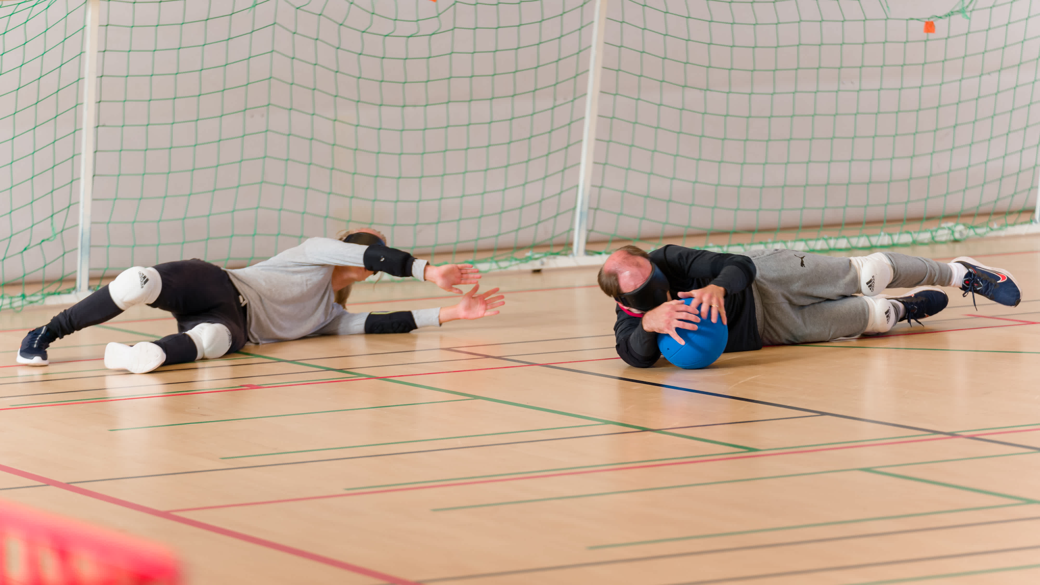 Två spelare har kastat sig liggande på golvet för att få tag i bollen, en av dem har fångat bollen med händerna.