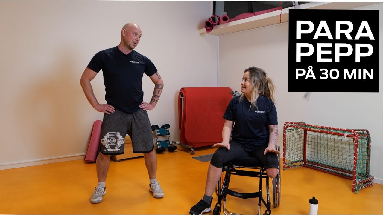 En man står bredvid en kvinna som sitter i rullstol. Mannen har skalligt huvud och mörka kläder, kvinna har blont hår som är uppsatt i en tofs, mörka kläder och ett amputerat ben.