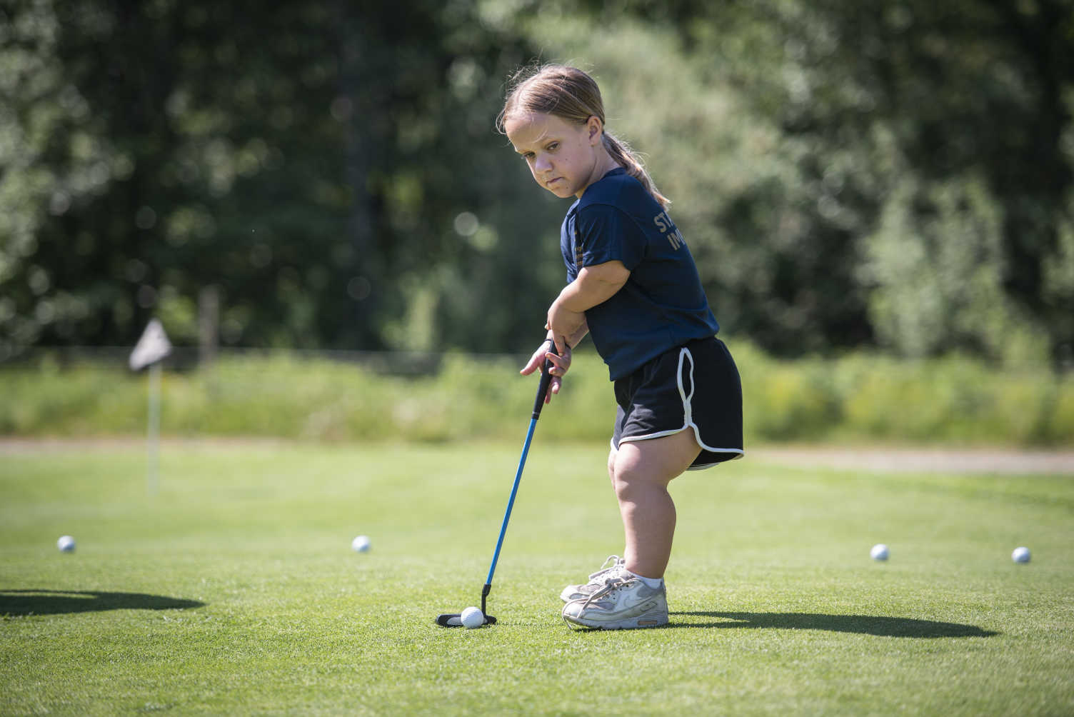 En ung tjej med kortväxthet puttar golfbollen.