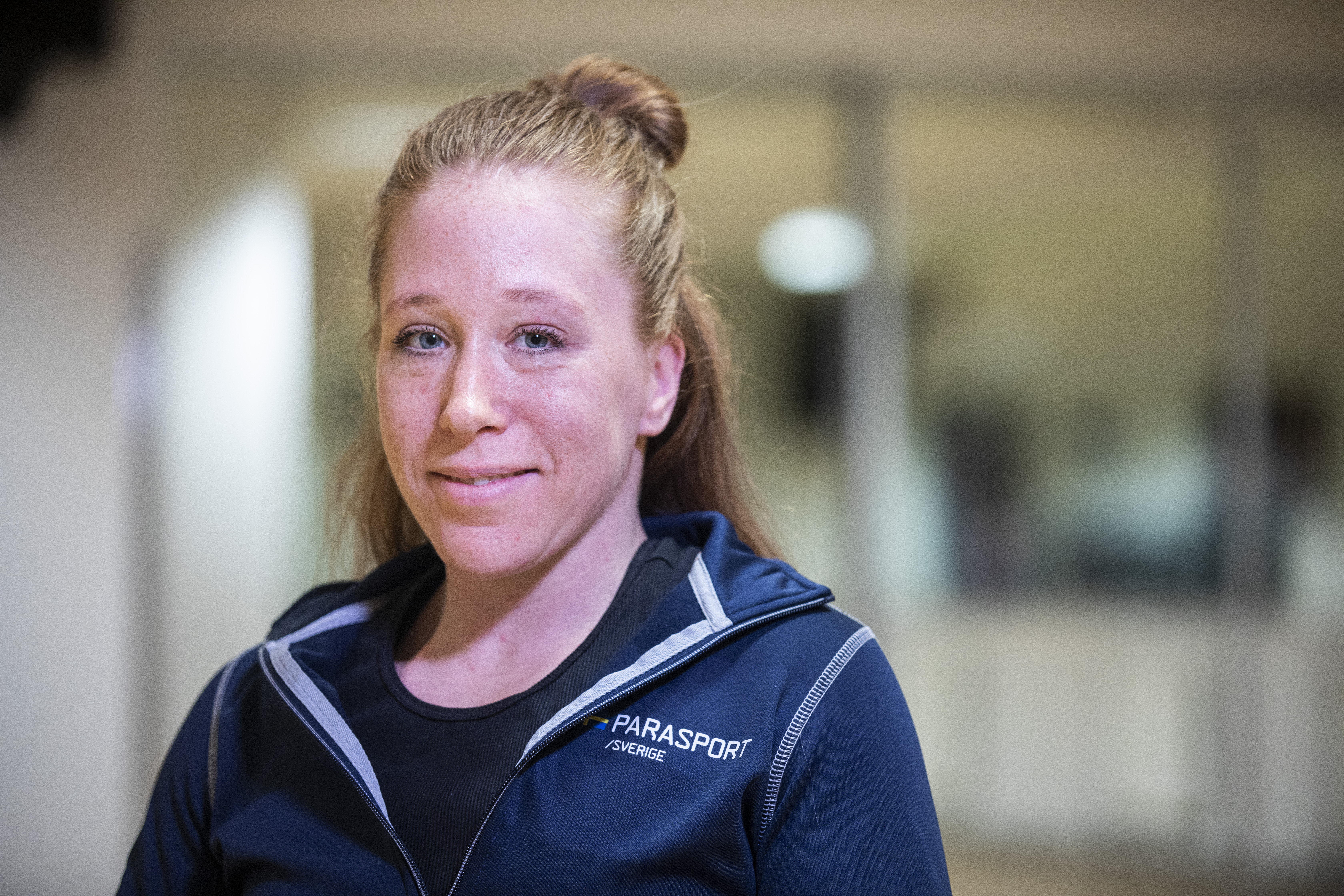 På bilden syns en kvinna med uppsatt, rödaktigt hår. En blå, långärmade tröja och hon tittar leende in i kameran. Bakgrunden är suddig.