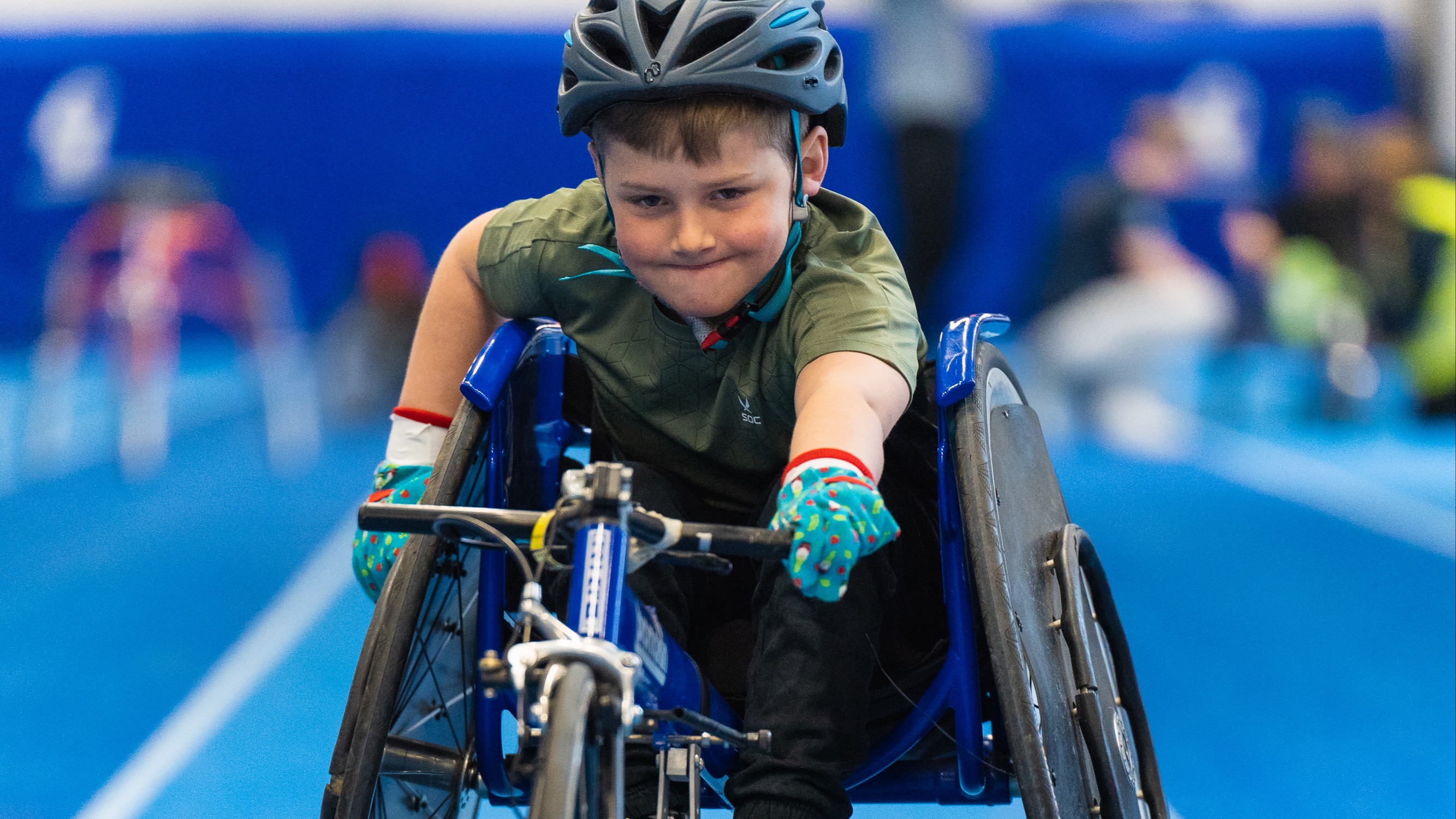 Inomhusmiljö, friidrottshall. Kille med cykelhjälm i friidrottsrullstol.