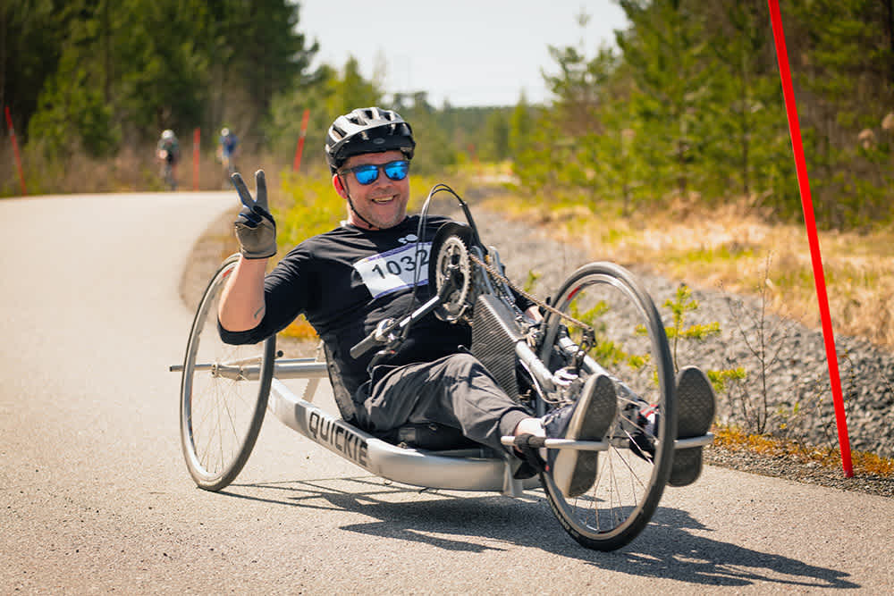En cyklist tittar in i kameran, ler och gör segertecknet.