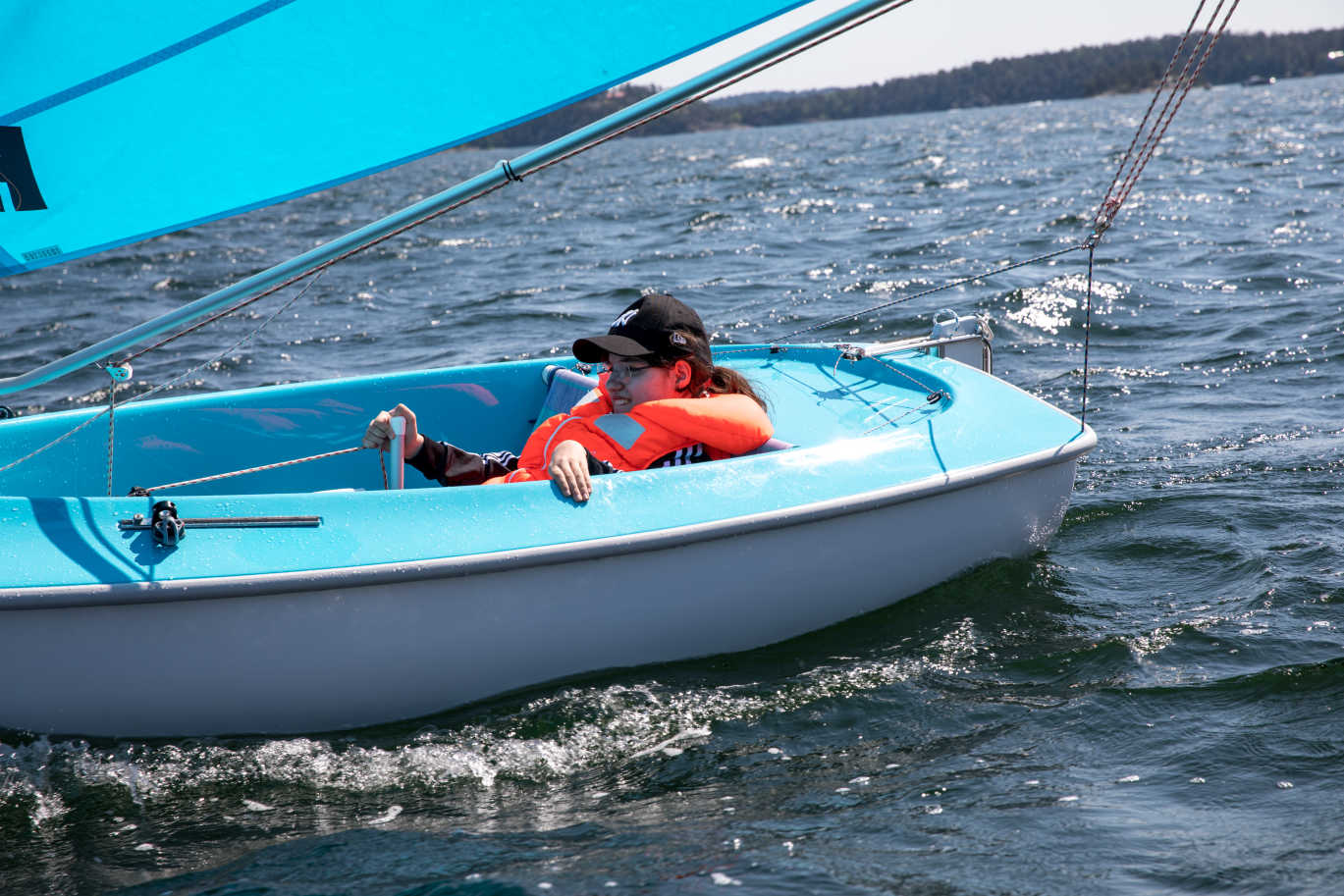 En person sitter i en liten segelbåt och styr båten.