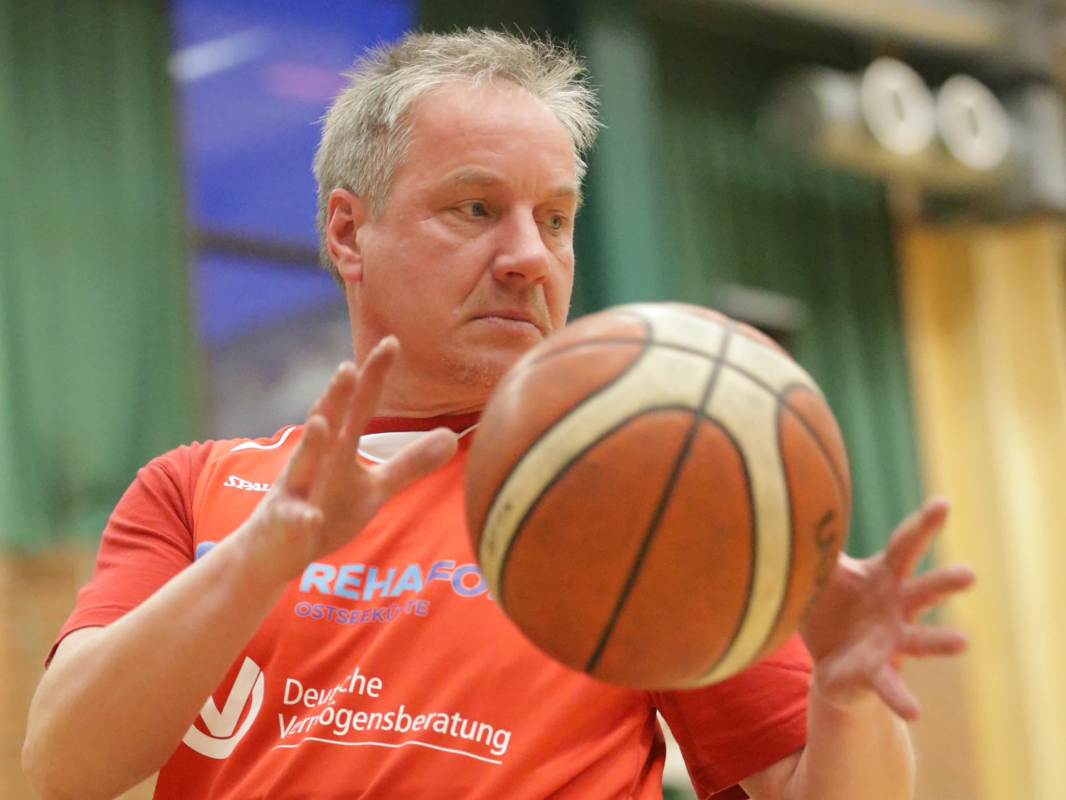 En äldre person i rullstol fångar basketbollen.