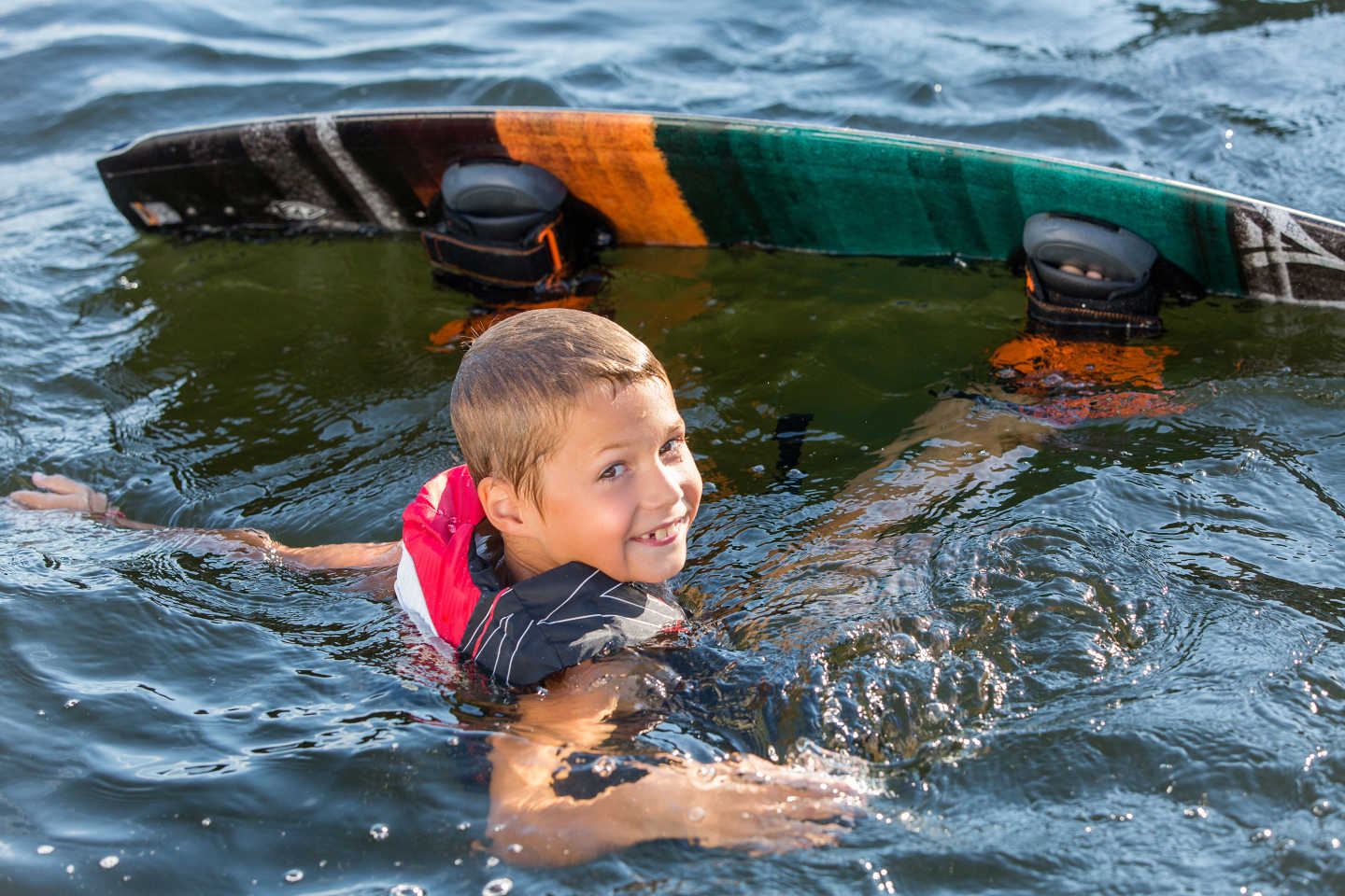 En ung pojke i vattnet med wakeboard på fötterna. Han ler in i kameran.
