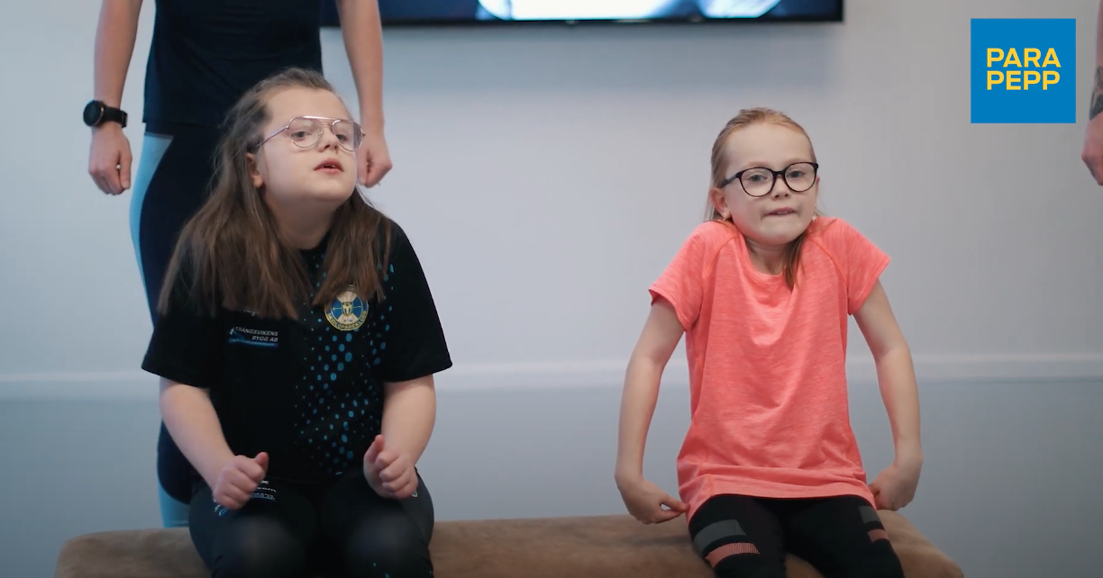 Meja och Hilda gör uppvärmningsövning genom att dra upp axlarna mot öronen.