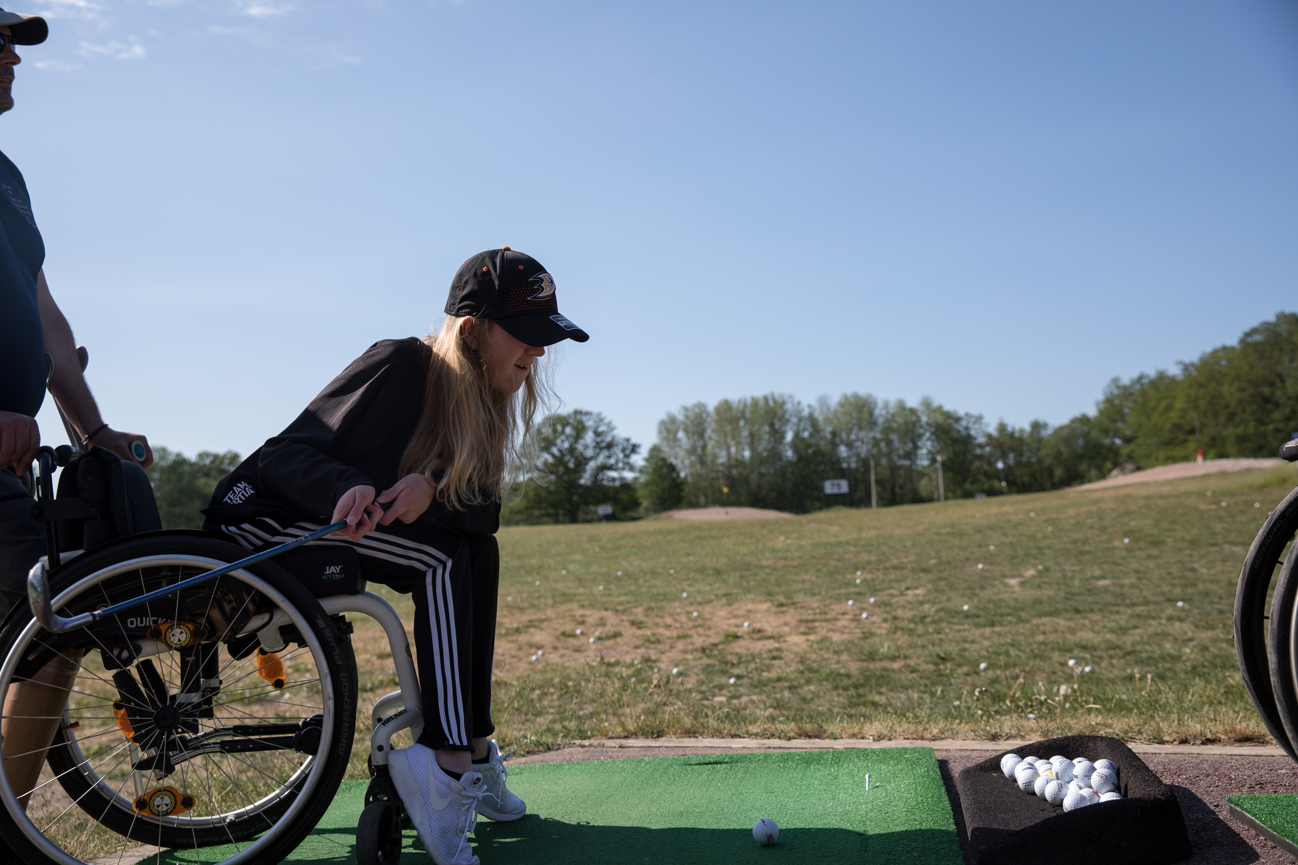 Tjej i rullstol svingar klubban för att slå ut bollen på golfbanan.