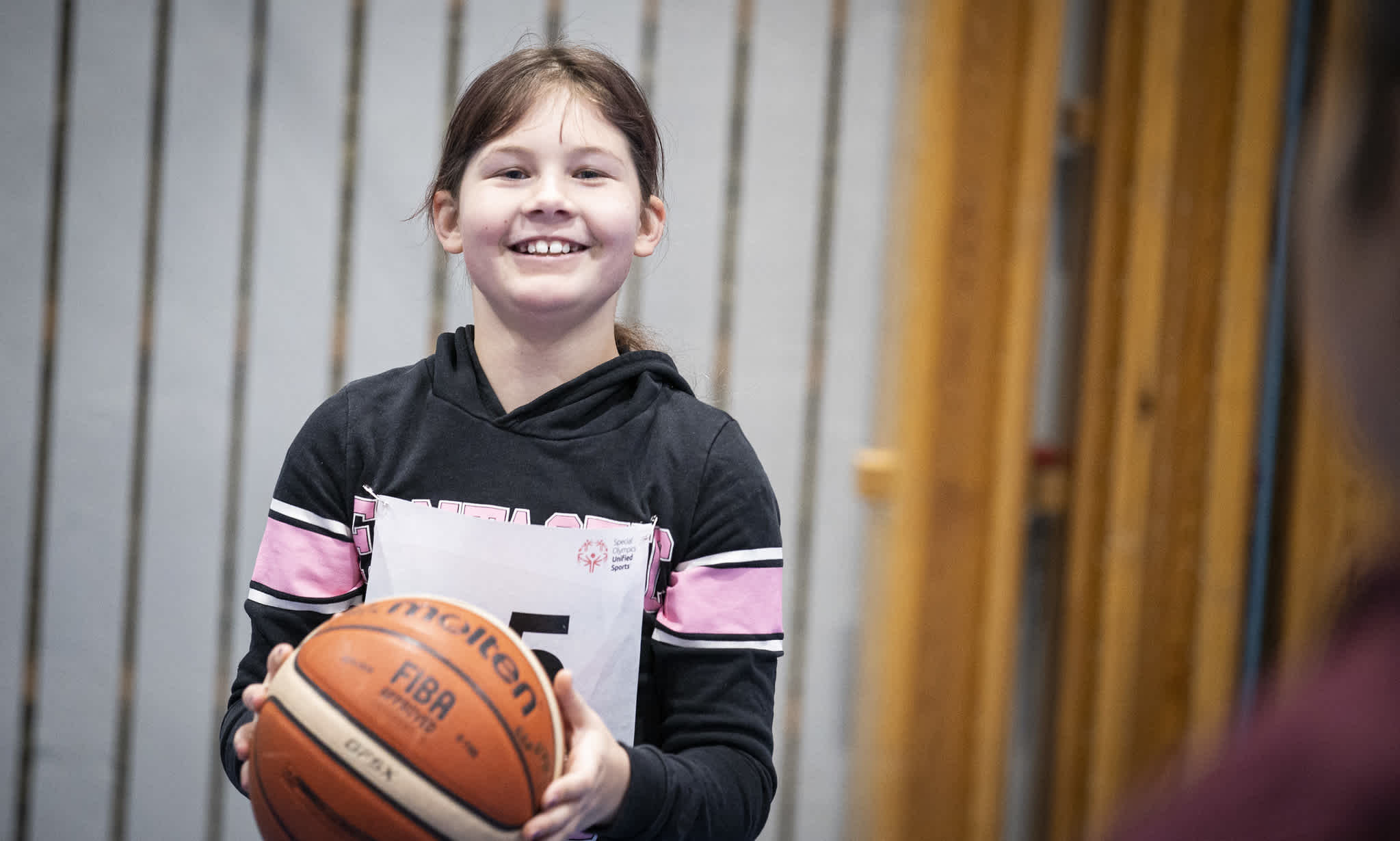 Ung glad tjej håller en basketboll.