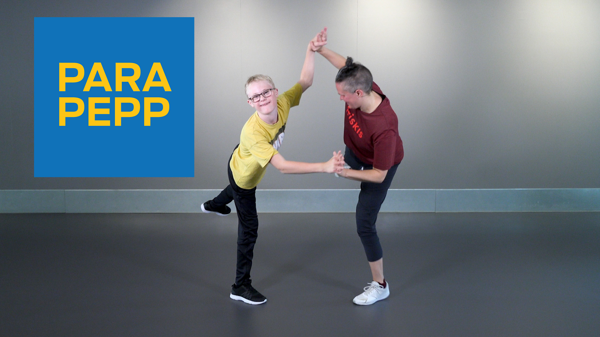 Två personer tränar tillsammans. De står på ett ben och håller varandra i händerna.