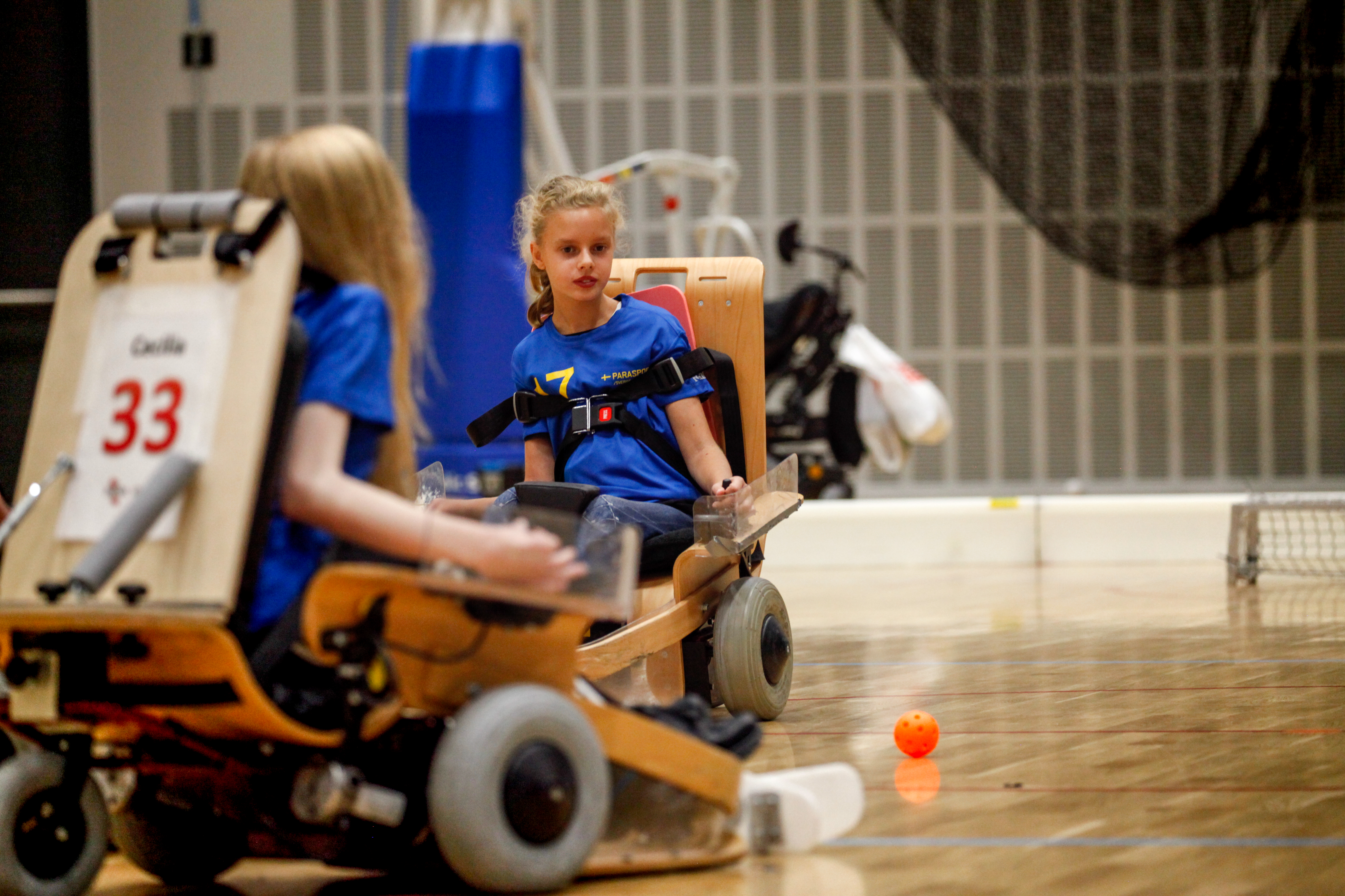 Två tjejer i elinnebandystol tävlar om att ta bollen.