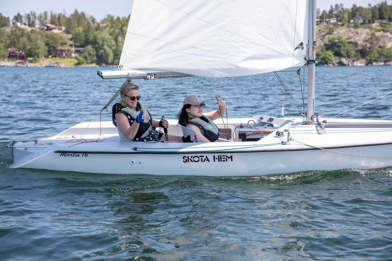 Två kvinnor sitter i en segelbåt och gör tummen upp.