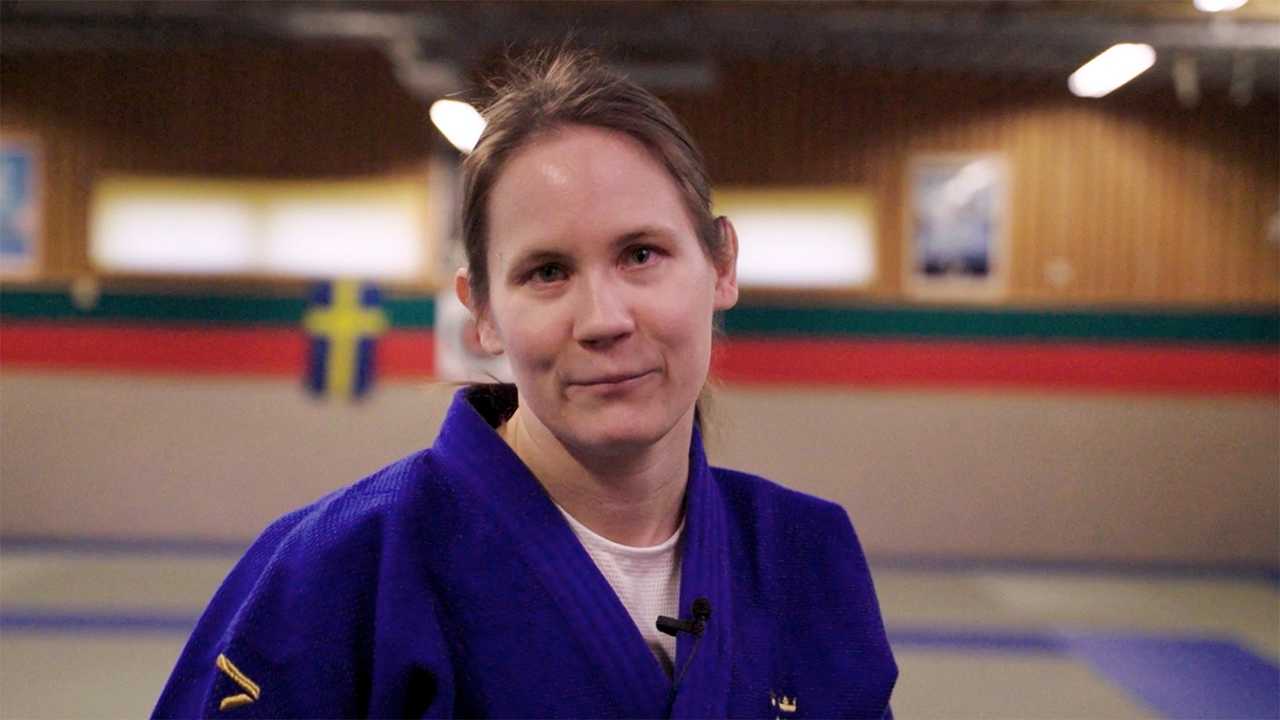 Inomhusmiljö, judosal. Kvinna i 30-årsåldern med brunt hår och blå judodräkt.