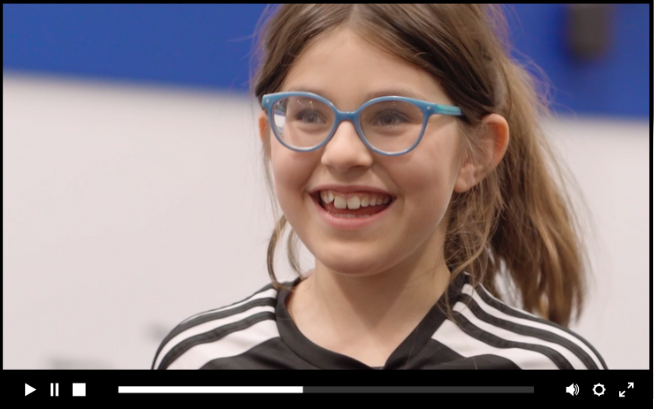 Närbild på ung flicka med träningskläder, brunt hår och glasögon.