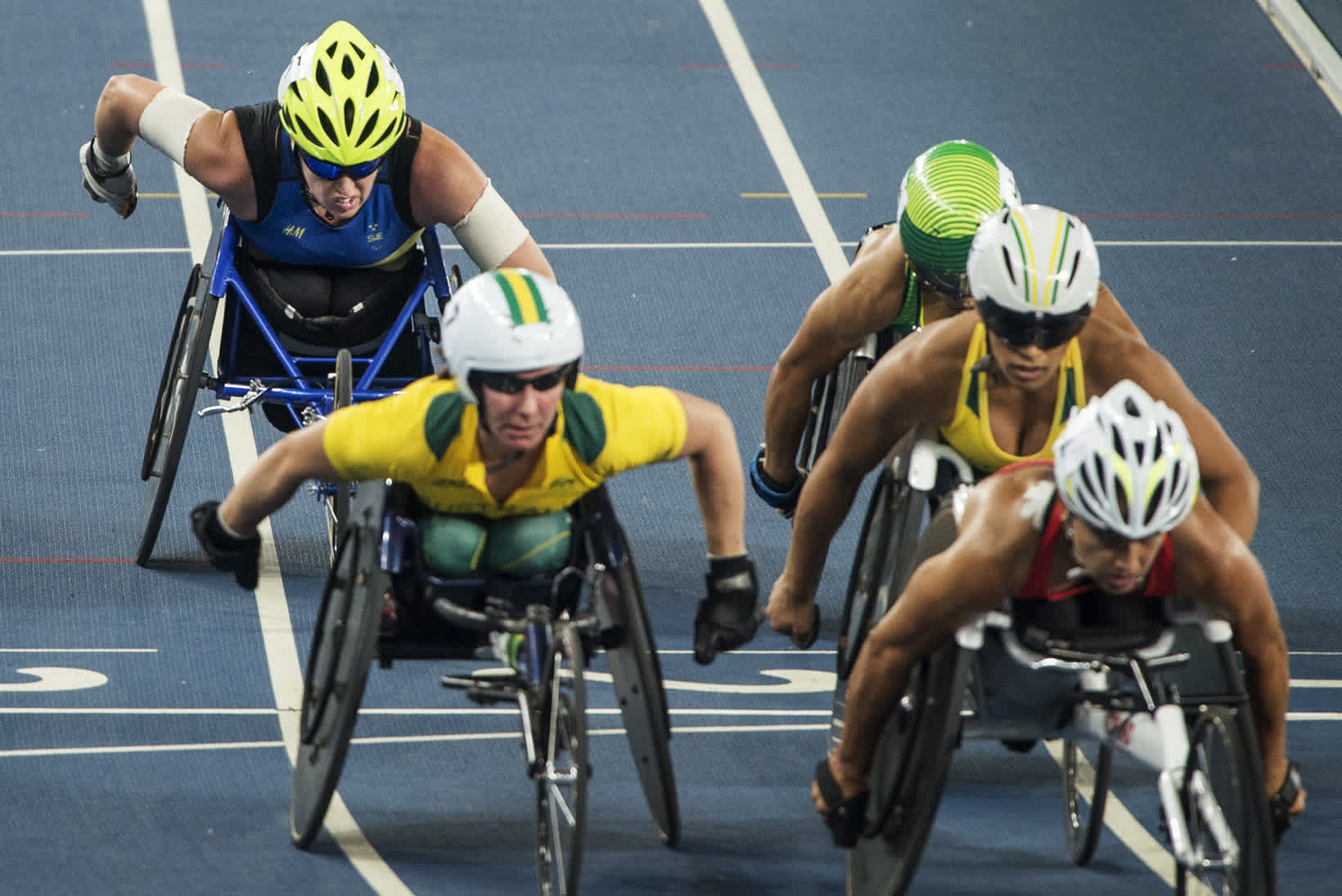 Fem kvinnor tävlar i att köra rullstol snabbt på friidrottsbanan. 