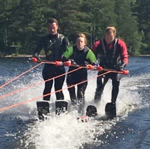 Tre personer på rad åker vattenskidor. De håller i en tredelad bom som drar dem framåt. 