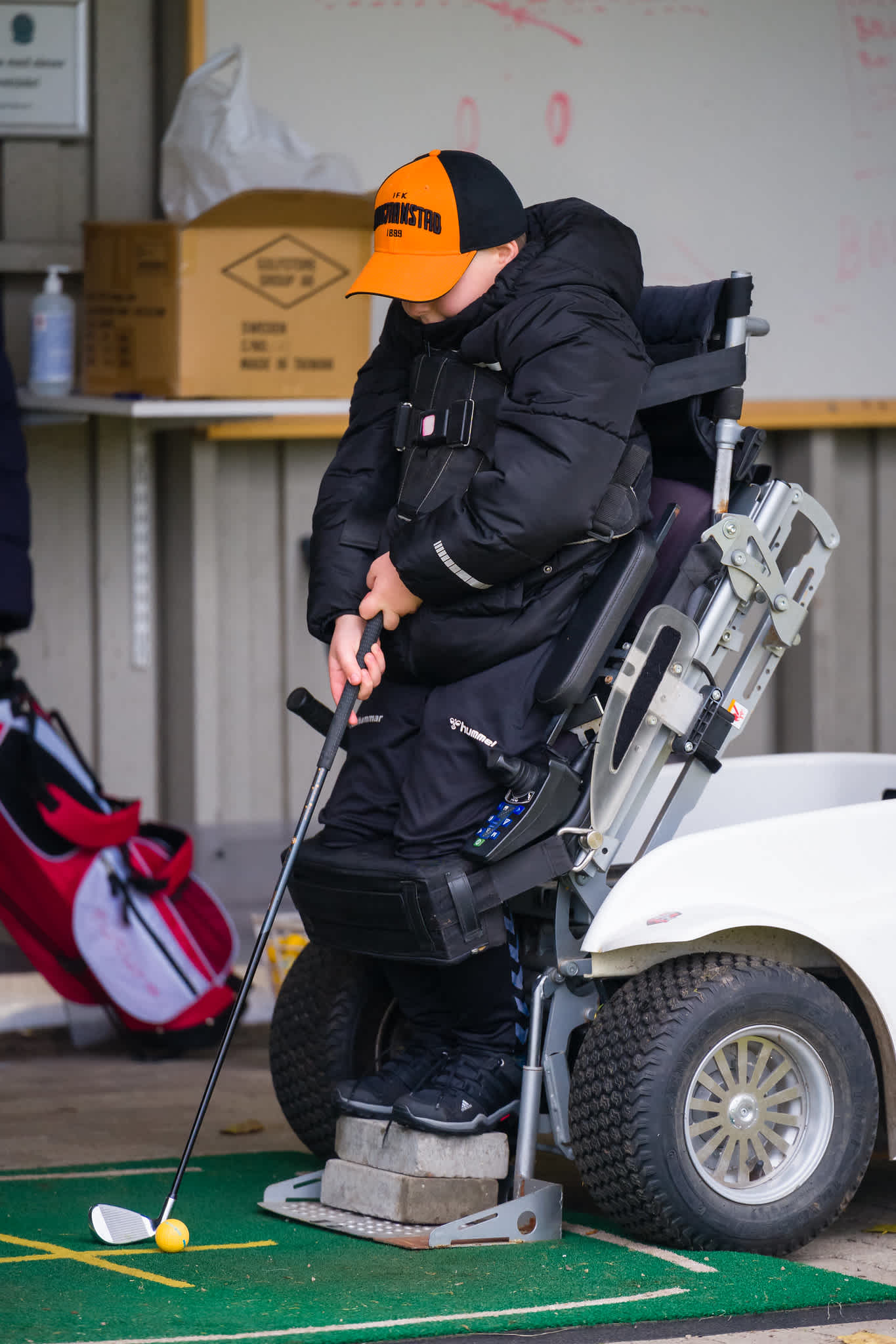 Pojke står med hjälp av en paragolfer vid utslagsplatsen och gör sig redo för att slå.