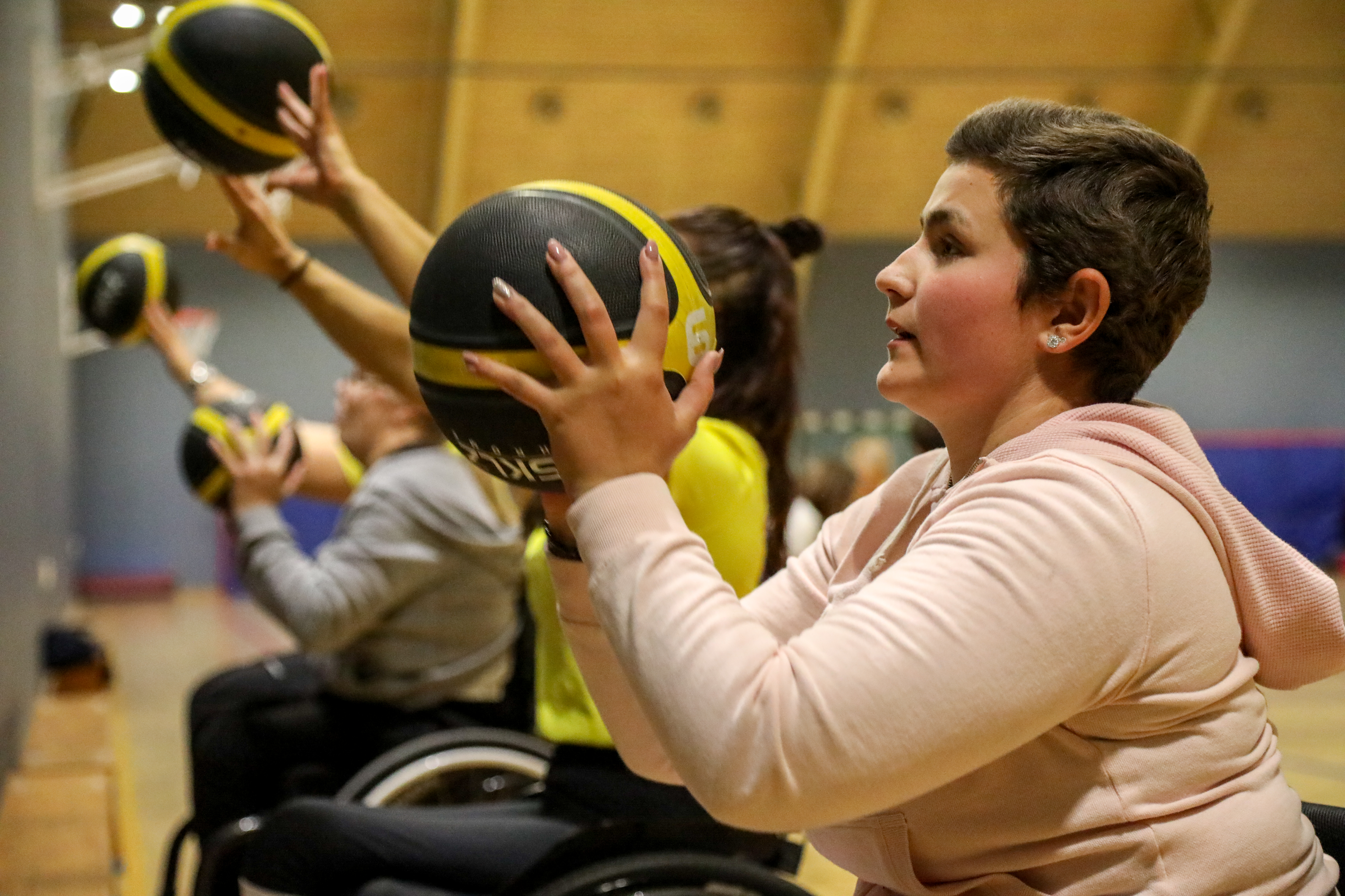 Ung kvinna kastar basketboll mot en vägg tillsammans med andra i bakgrunden.