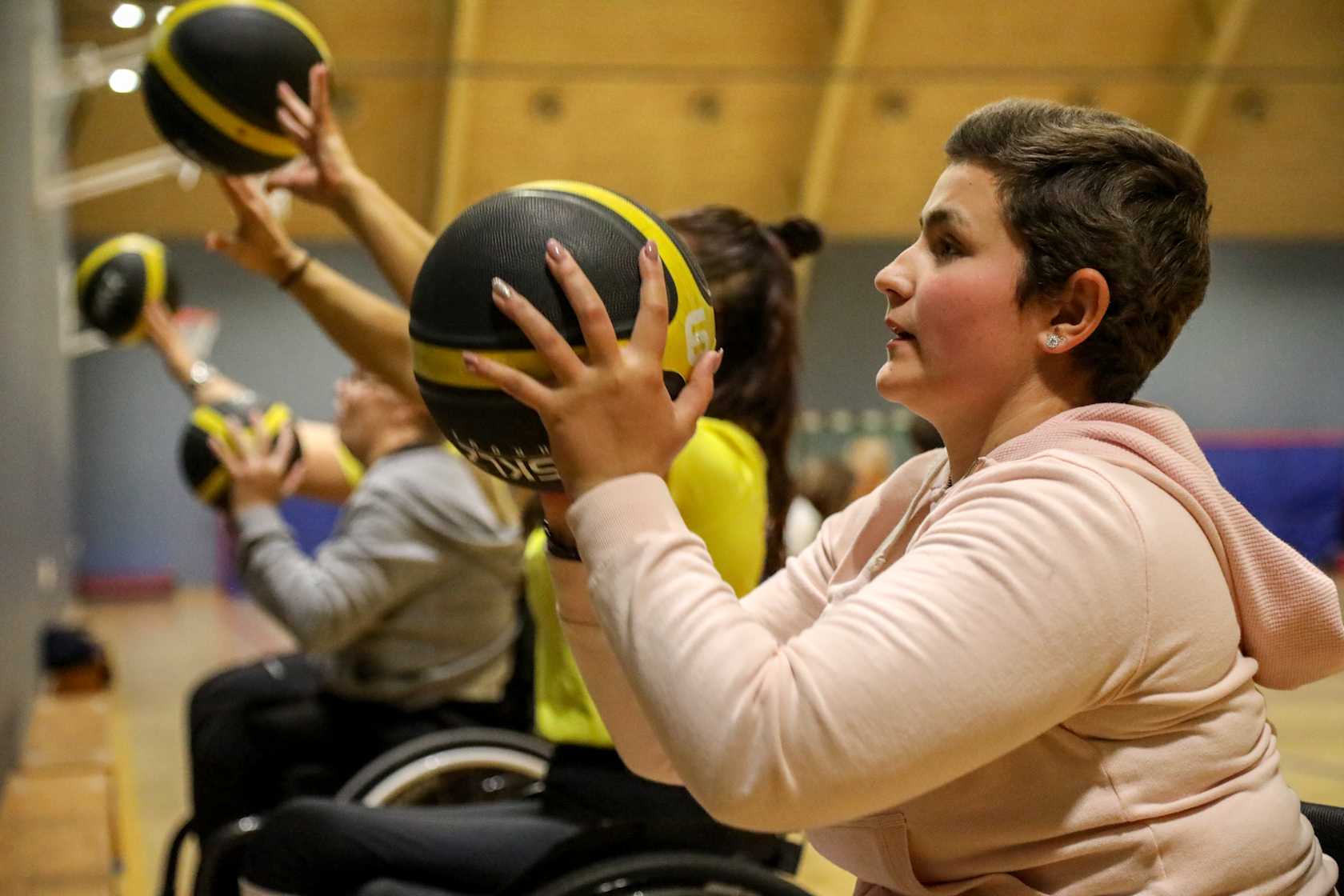 Ung kvinna kastar basketboll mot en vägg tillsammans med andra i bakgrunden.