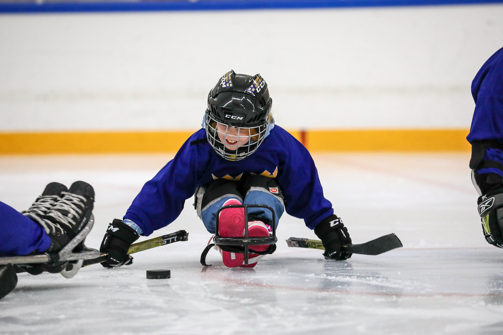 En kille i kälke tar sig framåt med hjälp av två korta klubbor.