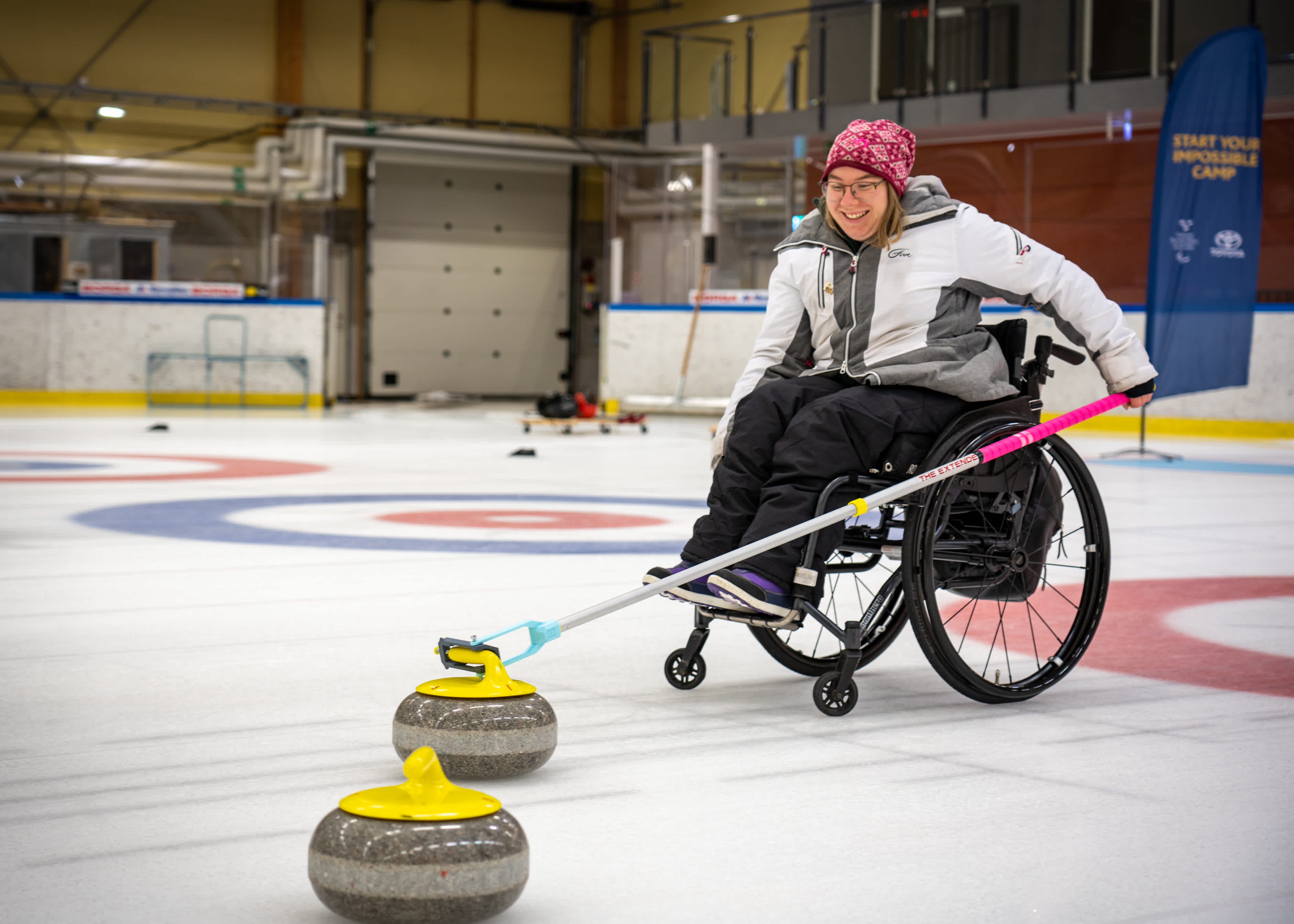 En ung tjej i rullstol curlar iväg en curlingsten.