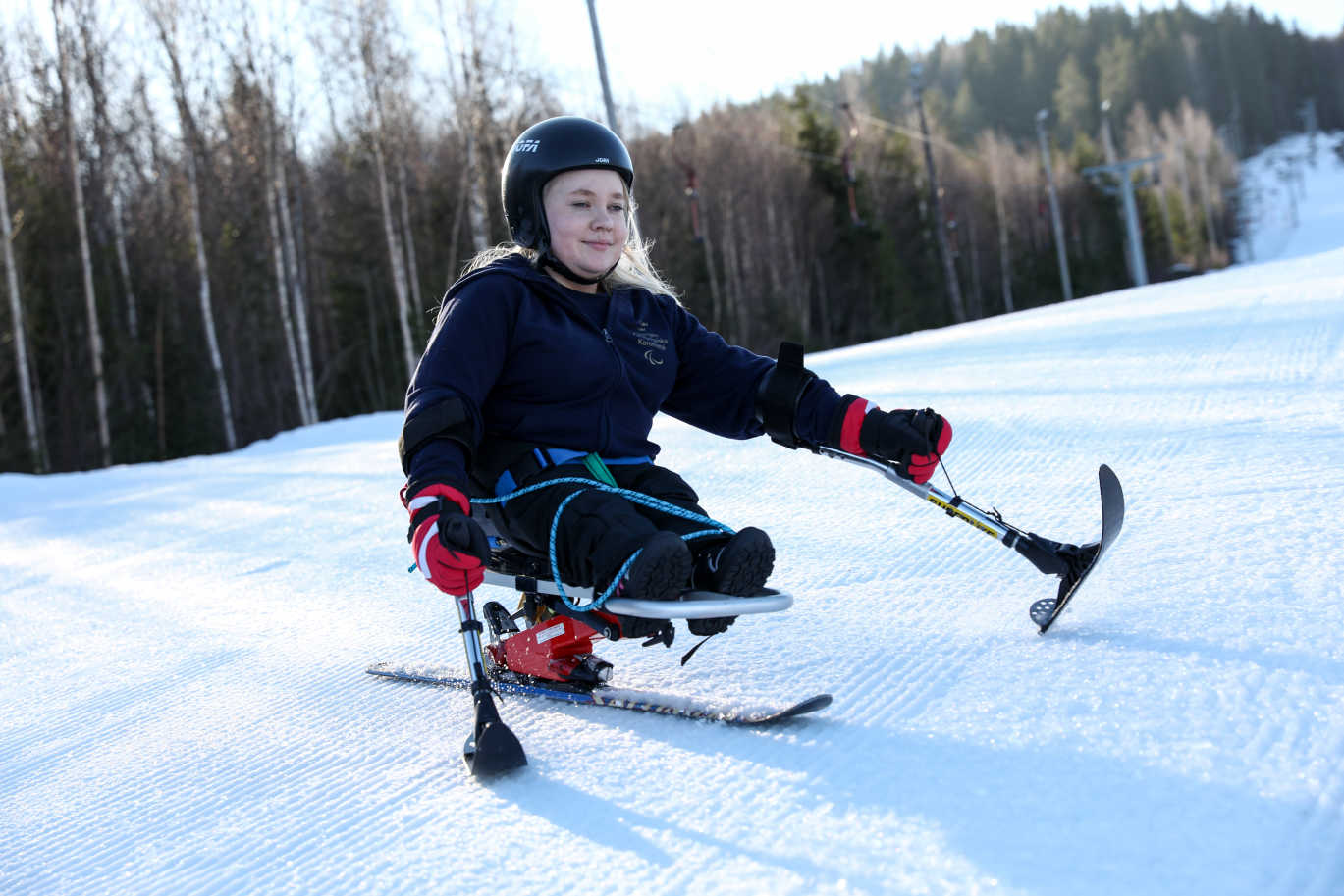 En tjej i sitski åker ner i skidbacken.