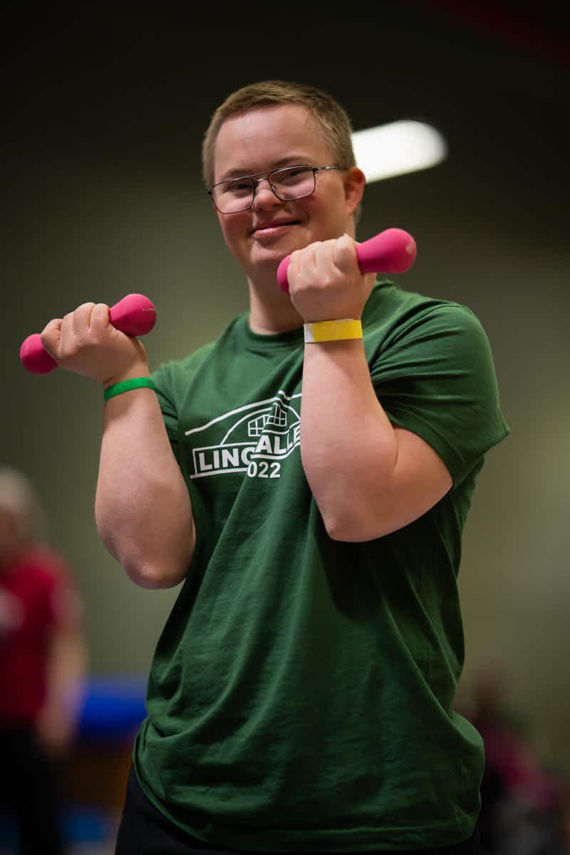 En kille tittar in i kameran och ler. Han håller rosa hantlar i händerna.