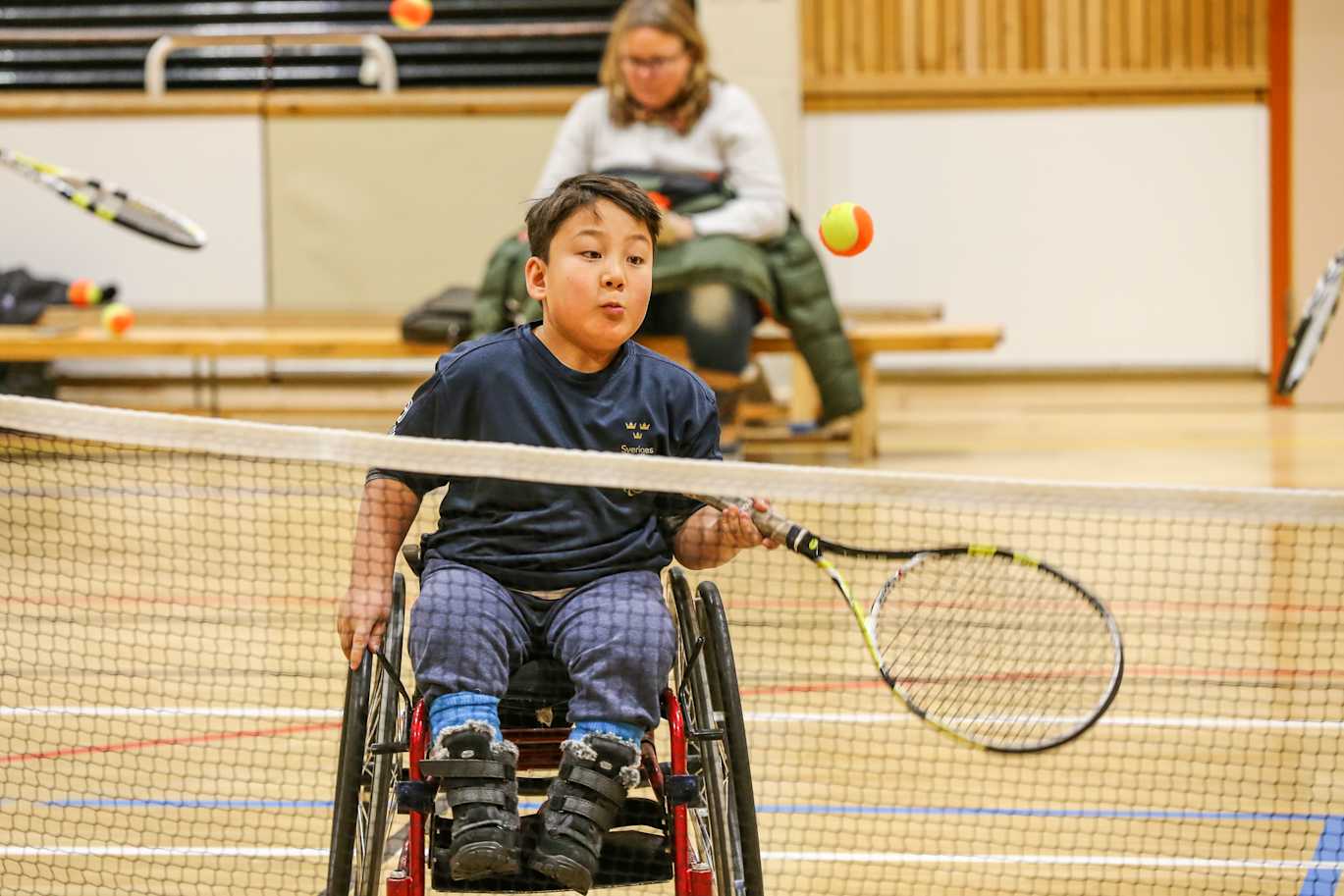 Pojke i rullstol ska precis slå tillbaka tennisbollen med en forehand.