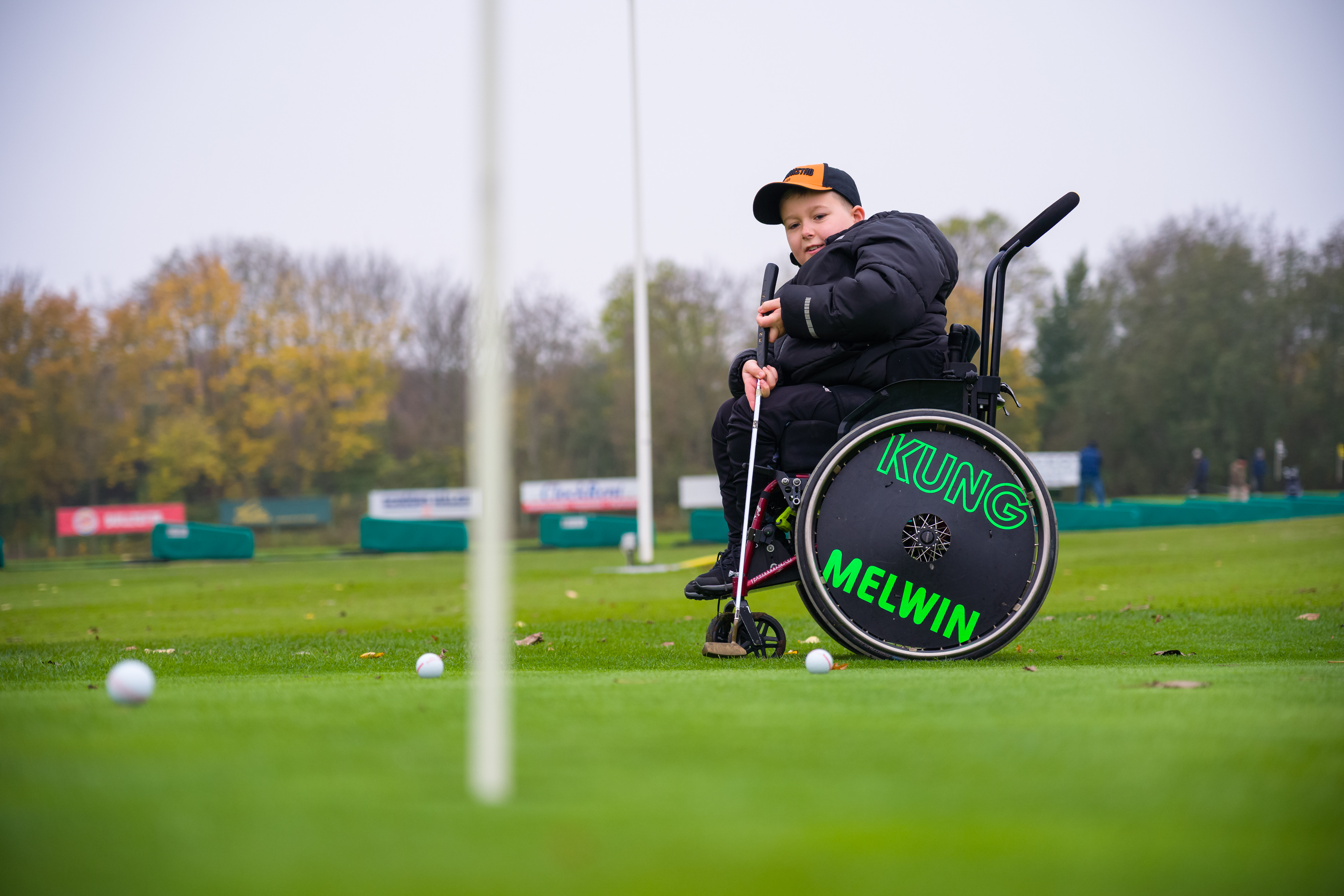 Pojke sitter i rullstol uppe på green och övar puttar.