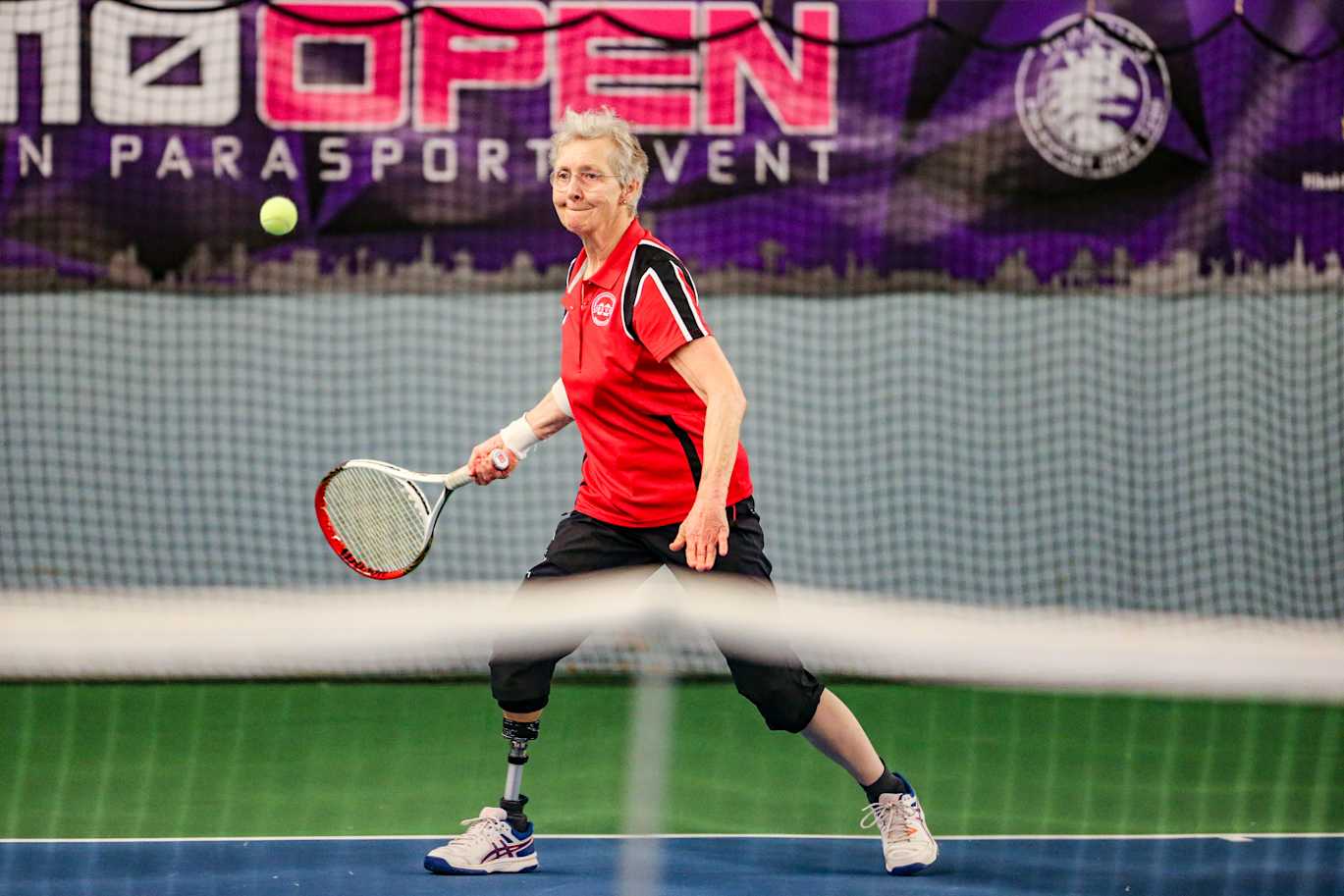 En kvinna med benprotes slår iväg en tennisboll.