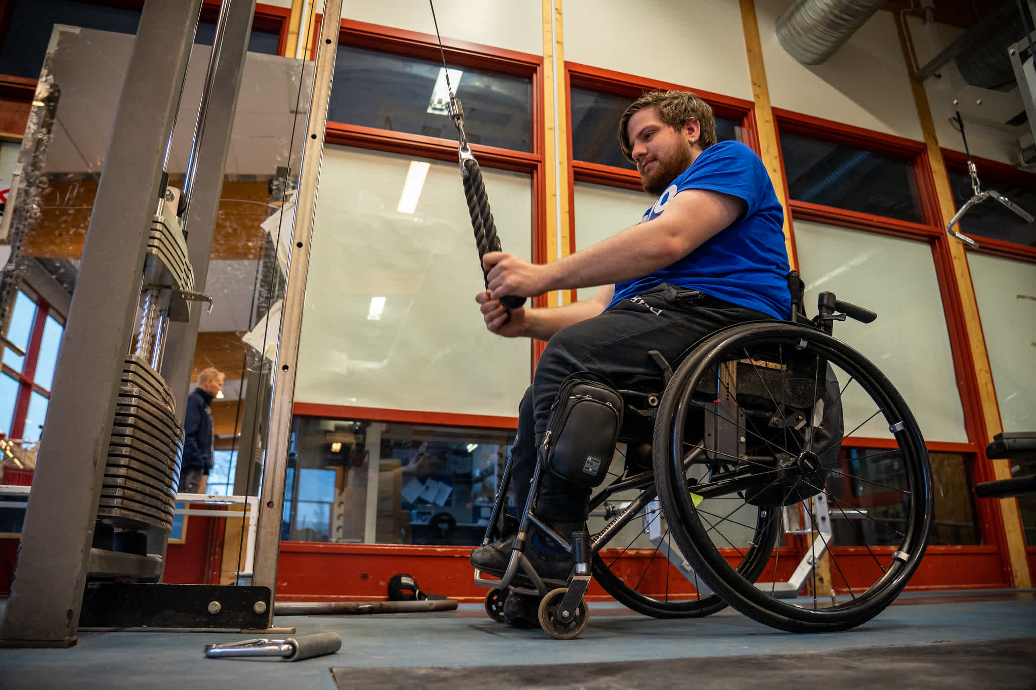 Man använder en stakmaskin på ett gym, sittande i rullstol.
