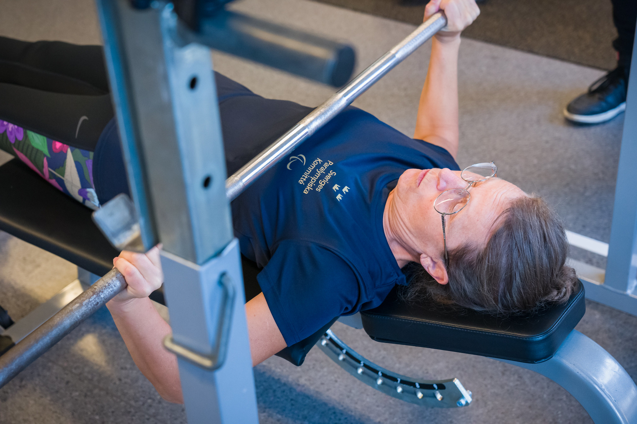 Kvinna ligger på bänken och fokuserar för att strax pressa stången med vikter uppåt.