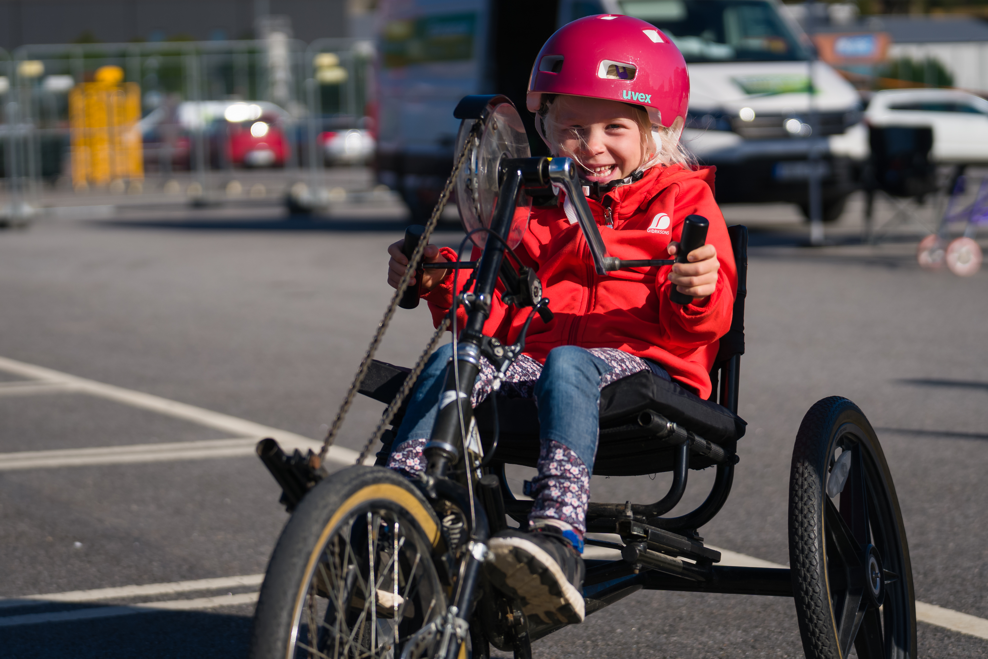 Liten flicka som ler mot kameran cyklar på en armcykel ute i solen.