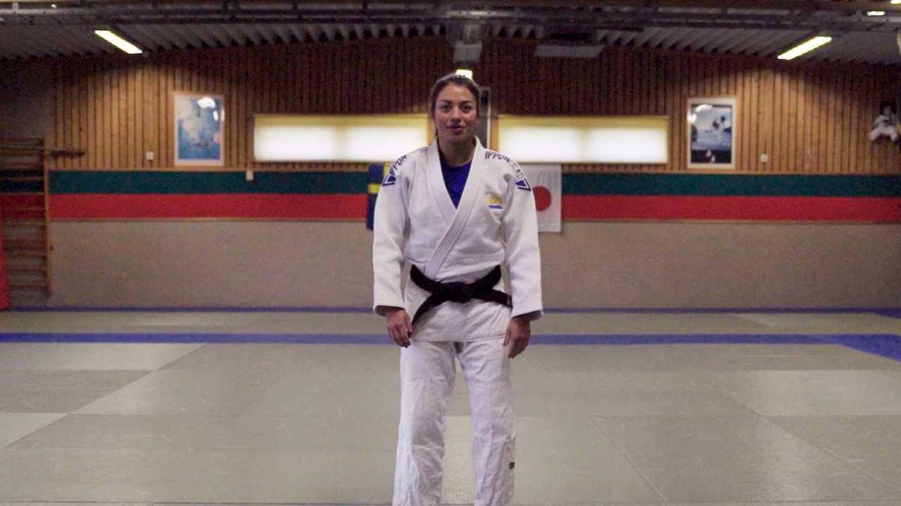 Inomhusmiljö, judosal. Kvinna i judodräkt står på mattan.