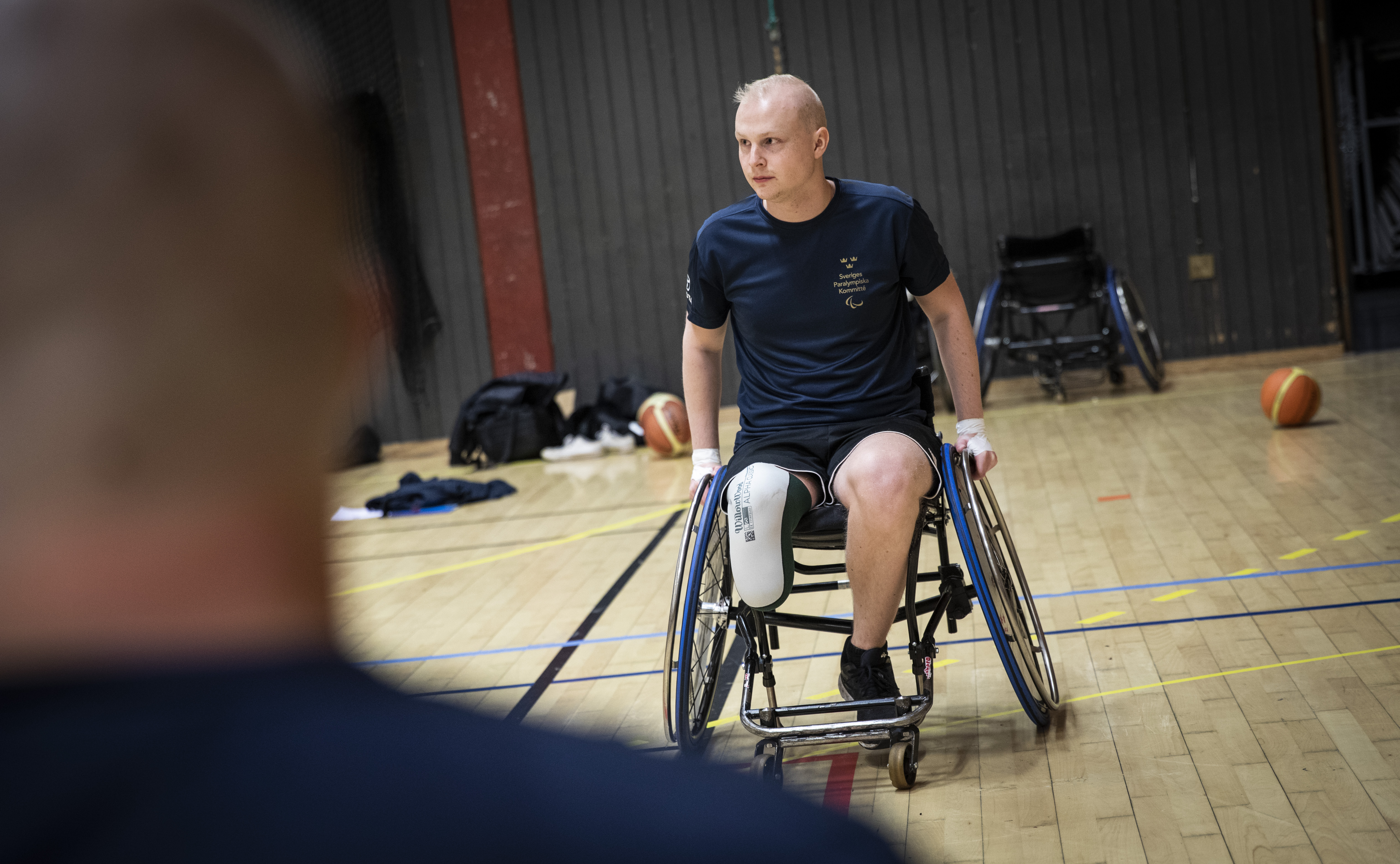 Ung man med benprotes i rullstol på en basketplan.