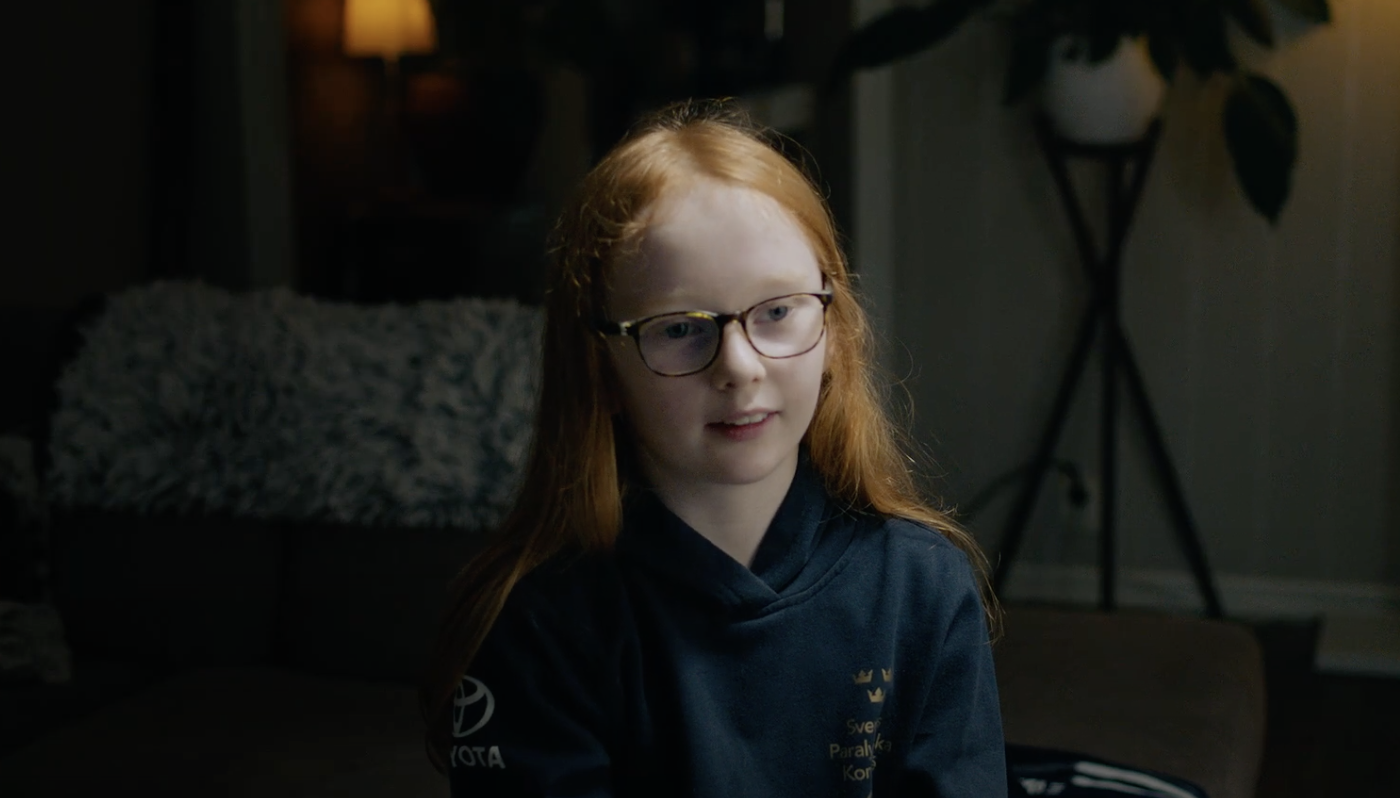 En skärmdump på Hillevi från filmen. Hon har rött hår och glasögon, hon sitter framför kameran i en soffa och blir intervjuad. Miljön är mörk och hon är belyst med en studiolampa på sin vänstra sida.