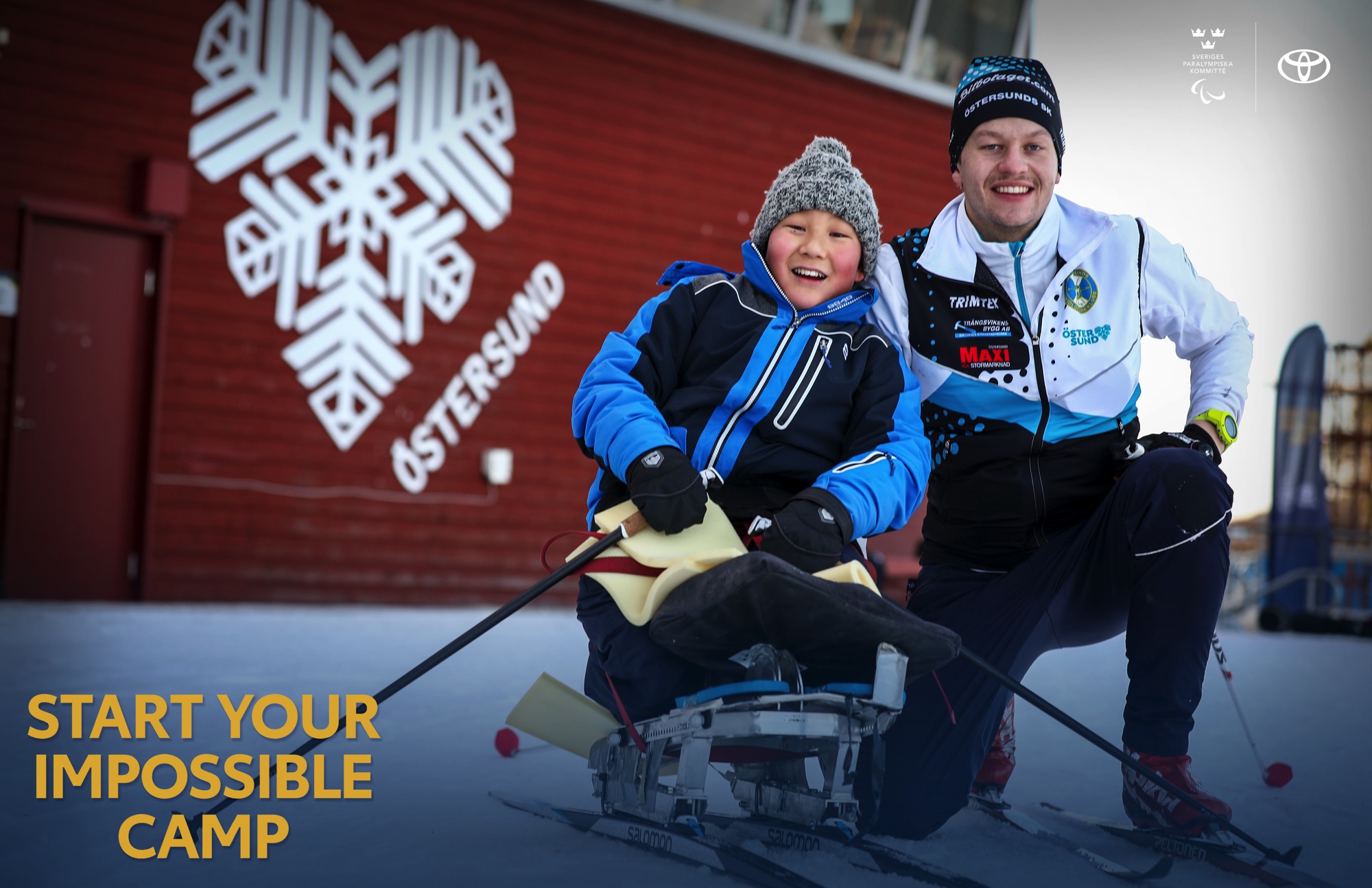 Utomhusmiljö. En pojke i sitski och en ledare på huk på en snötäckt plan, framför ett rött hus. På huset är det ett vitt hjärta och texten Östersund.