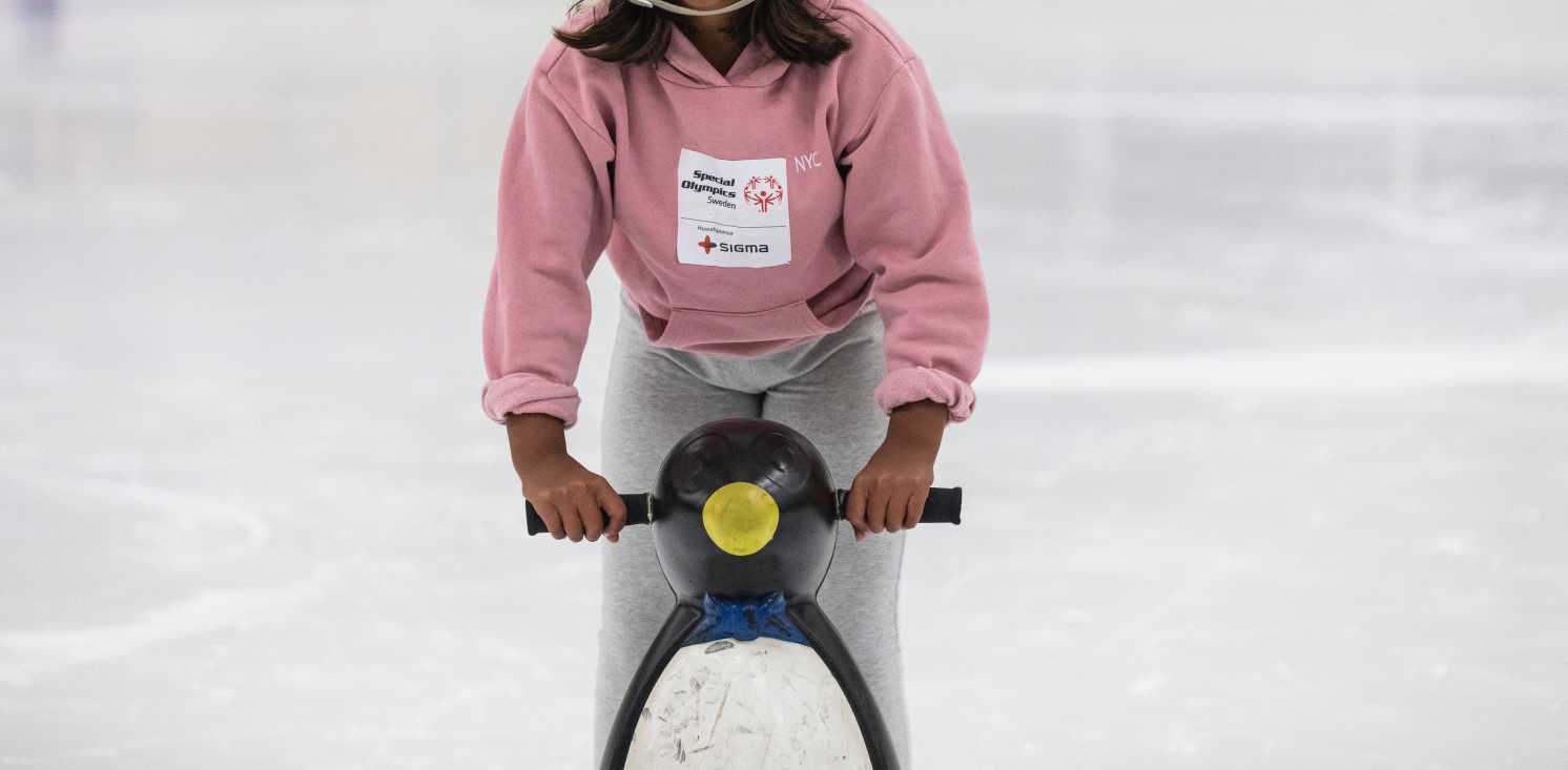 En tjej åker skridskor på isen med hjälp av ett balansstöd i form av en pingvin med handtag att hålla i.