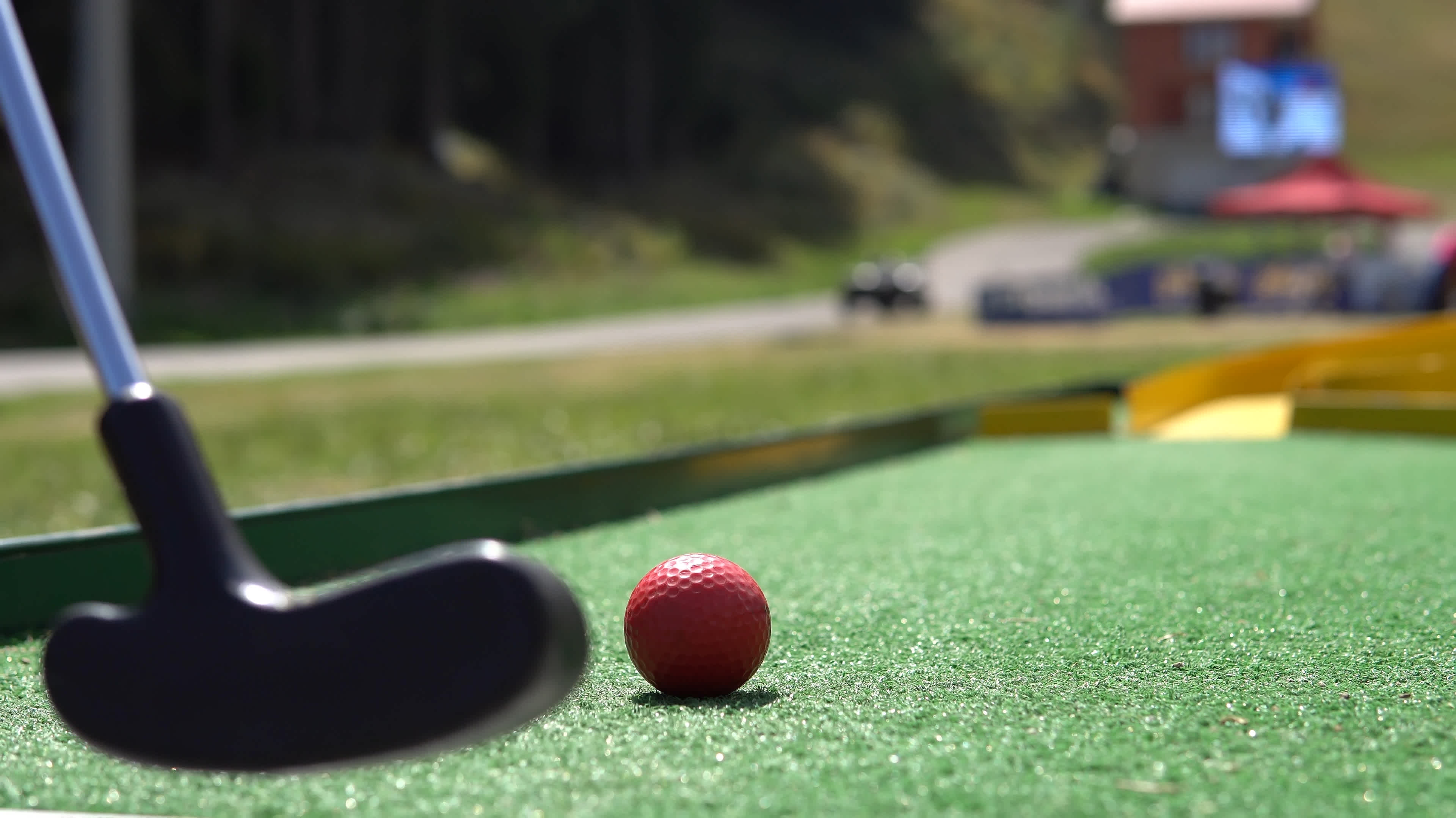 En bangolfklubba och en röd golfboll på en bangolfbana.