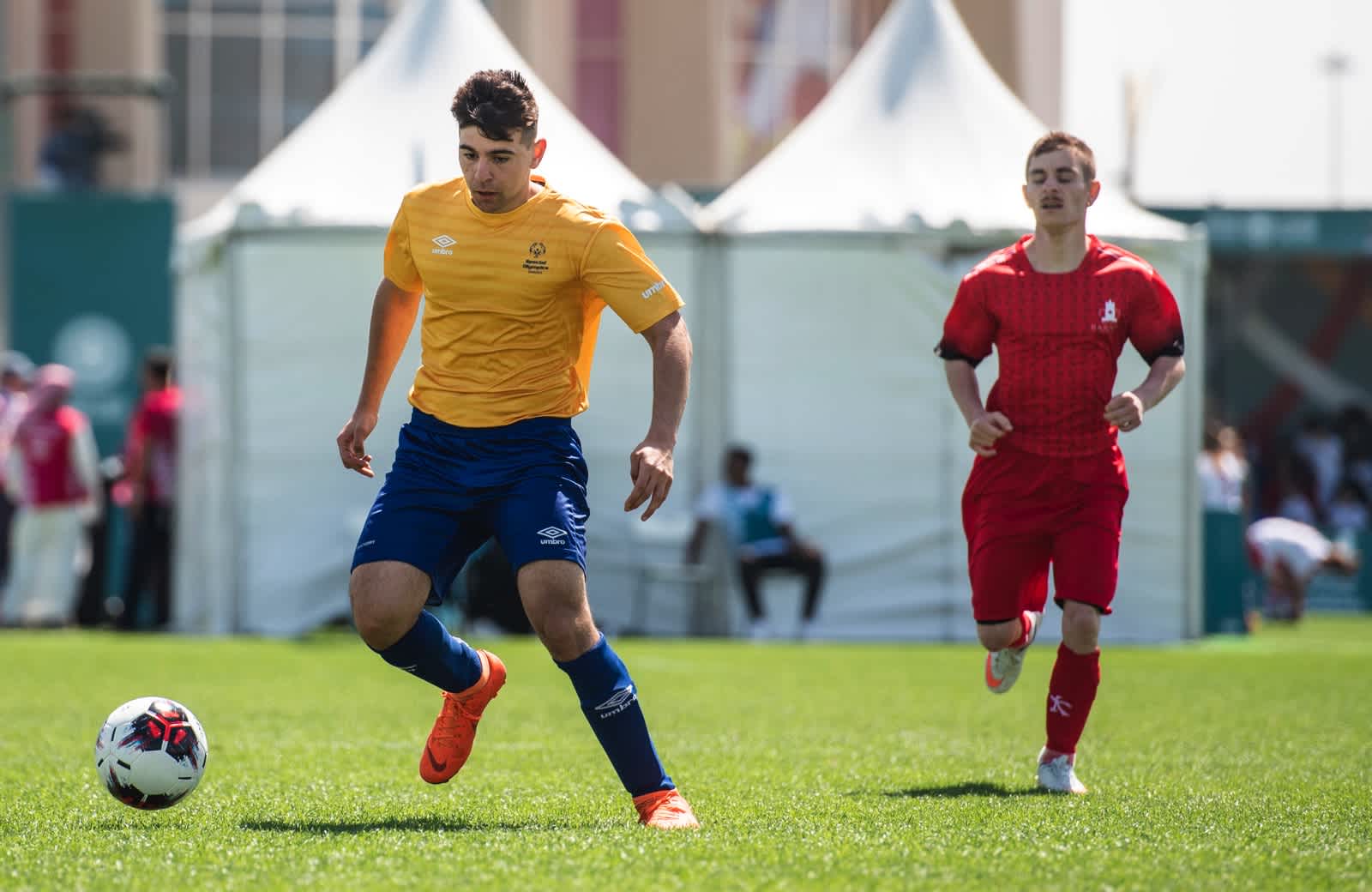 En fotbollsspelare springer med bollen. En motspelare jagar efter honom.